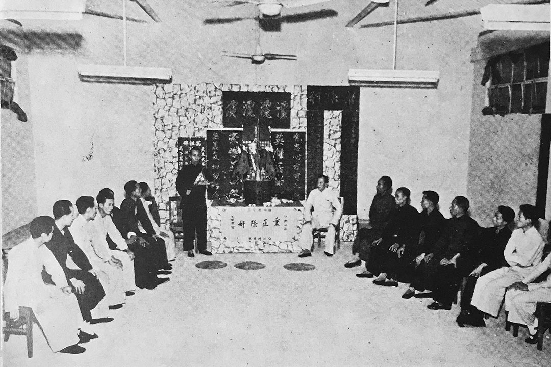 進入神壇後,龍頭(又稱坐館,祭壇左邊黑衣站立者)手執幫眾授權他的旗幟,為新成員舉行入會儀式。圖:《Triad Societies in Hong Kong》