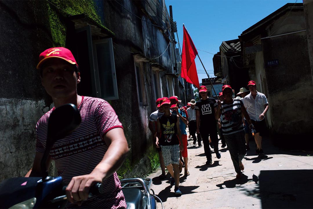 村民拿著國旗,沿村內小路走到舉行村民大會場。