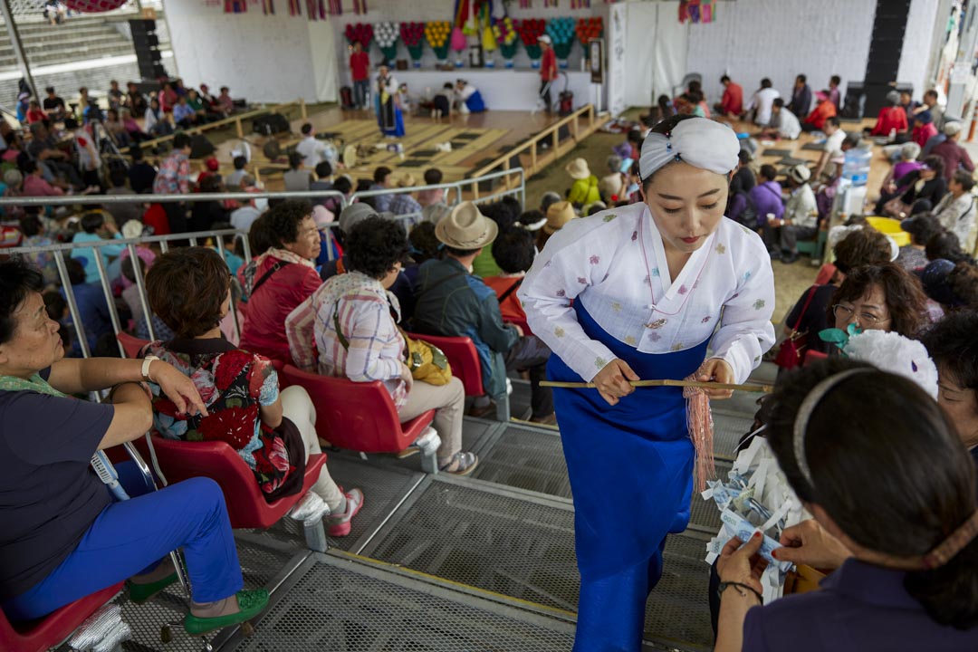 南韓江陵市,端午祭中一名年輕的薩滿巫師正在收集捐款。長達一個多月的端午祭為江陵市市民向山神祈求年年豐收的傳統習俗,於2005年成功向聯合國教科文組織將端午祭申報為非物質文化遺產。
