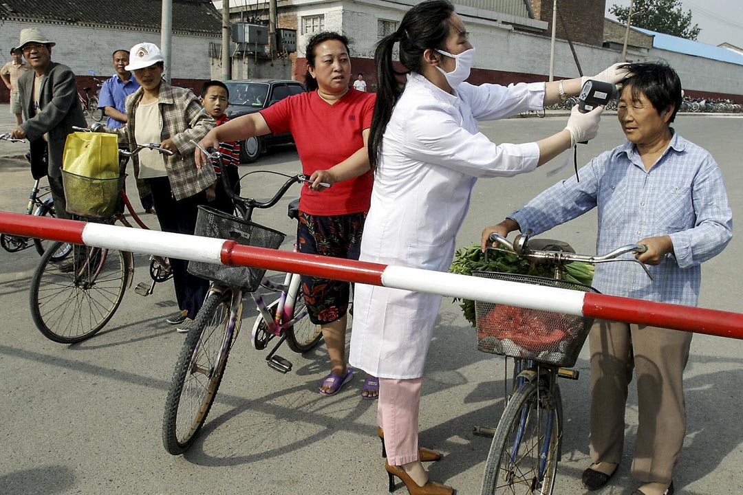 2003年6月8日,政府工作人員在通往北京居民區的路障前替進入的市民檢查體溫。