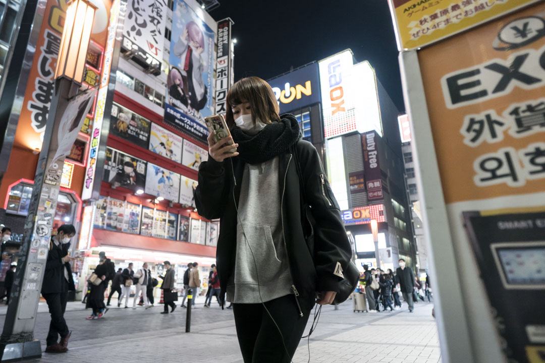 2020年2月13东京,戴著口罩的妇女使用智能手机。