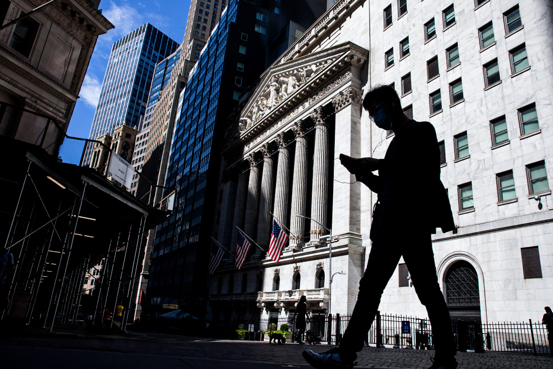 2020年7月20日,一名戴著口罩的行人在美國紐約證券交易所(NYSE)前經過時看著智能手機。