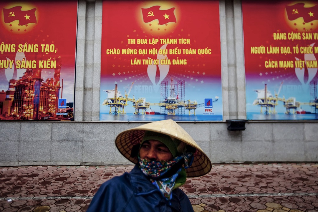 一名小販站在慶祝第十一屆越南人民代表大會舉行的海報前。