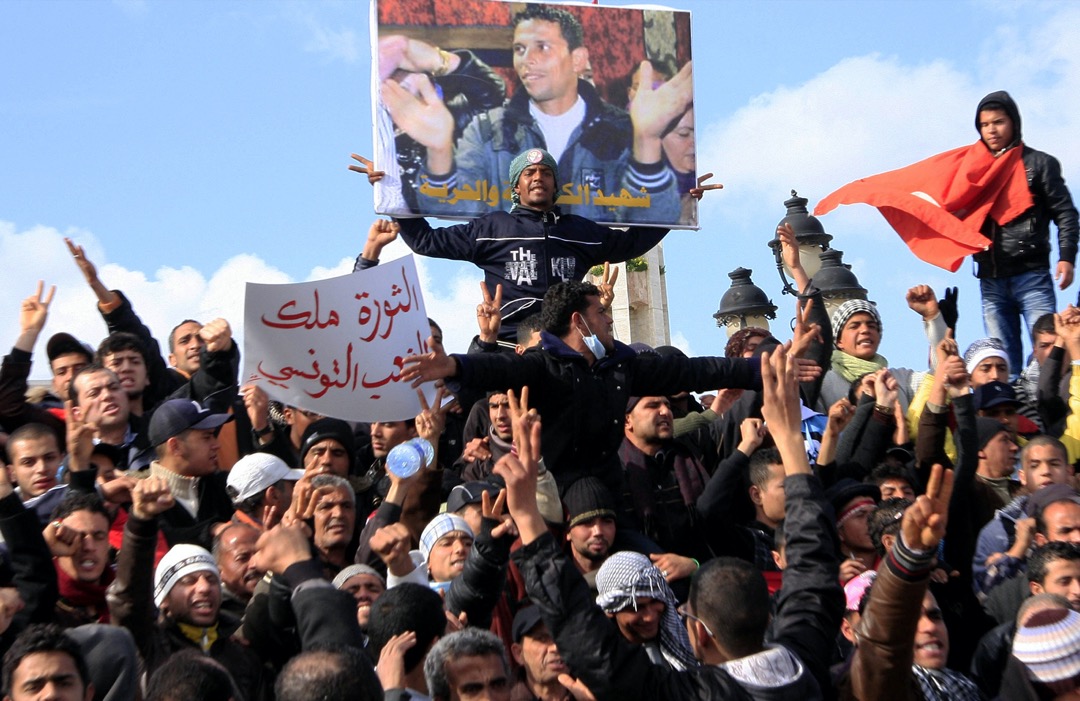 2011年1月28日,突尼西亚首都突尼斯,民众在政府宫外举起一幅布瓦吉吉(Mohamed Bouazizi)的肖像示威。26岁大学生布瓦吉吉早前到政府宫外自焚,抗议摆摊时受到警察滥用职权的欺侮。