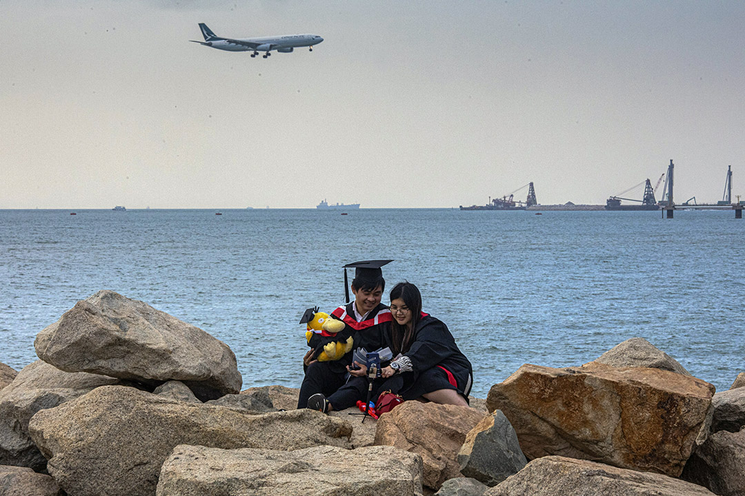 2020年11月30日香港国际机场外,一架国泰航空飞机降落,一对情侣拍毕业照。