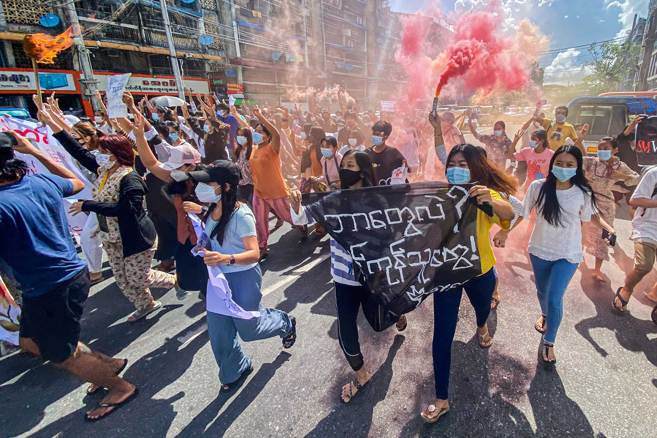 2021年7月14日缅甸仰光,反政变示威游行期间,妇女手持横幅和紧急信号棒奔跑。