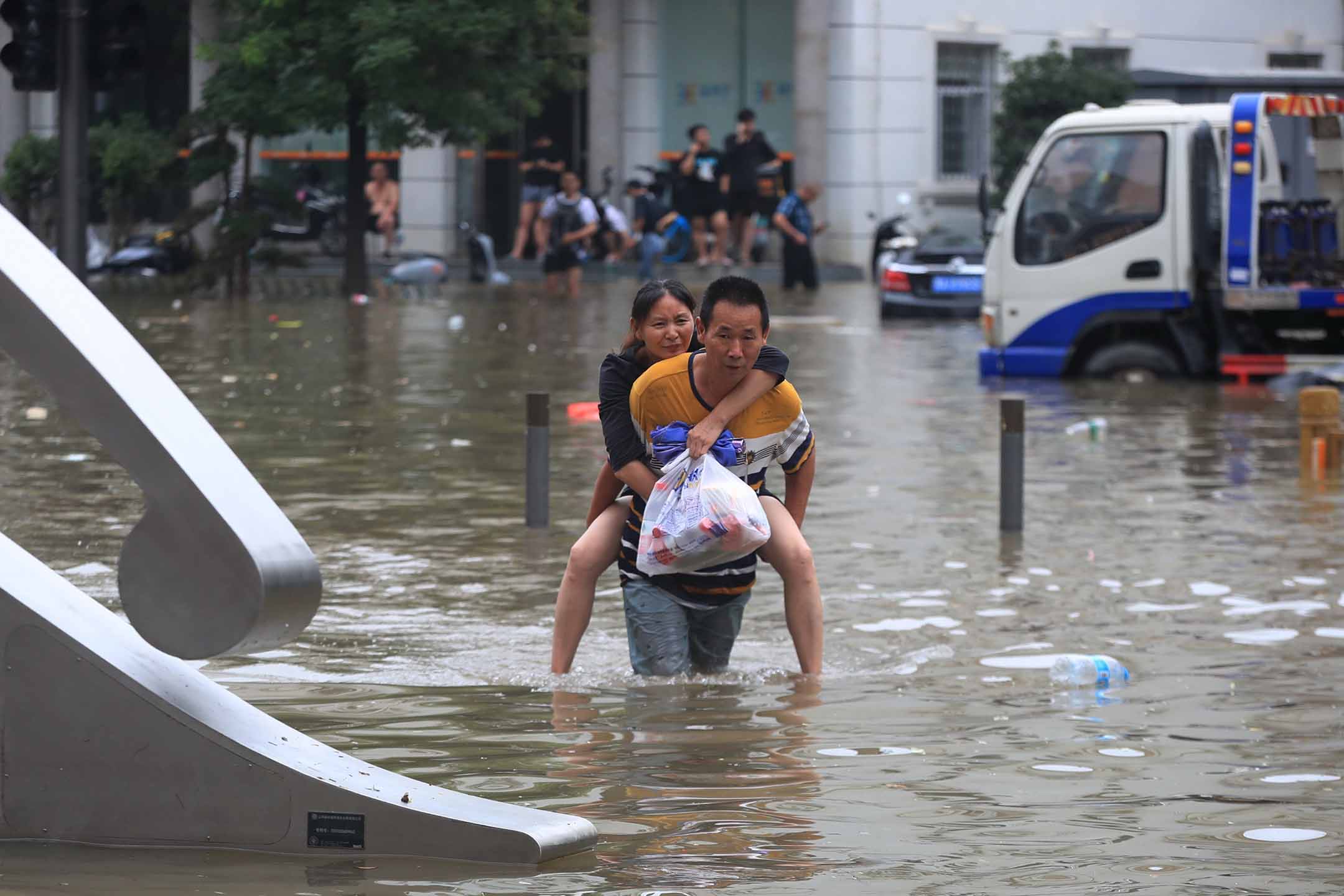 2021年7月20日中國鄭州，傾盆大雨後，一名男子在被洪水淹沒的道路上背著一名婦女。