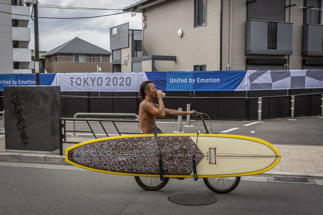 2021年6月28日日本藤澤市,一名衝浪者騎車經過東京奧運會的宣傳橫幅。