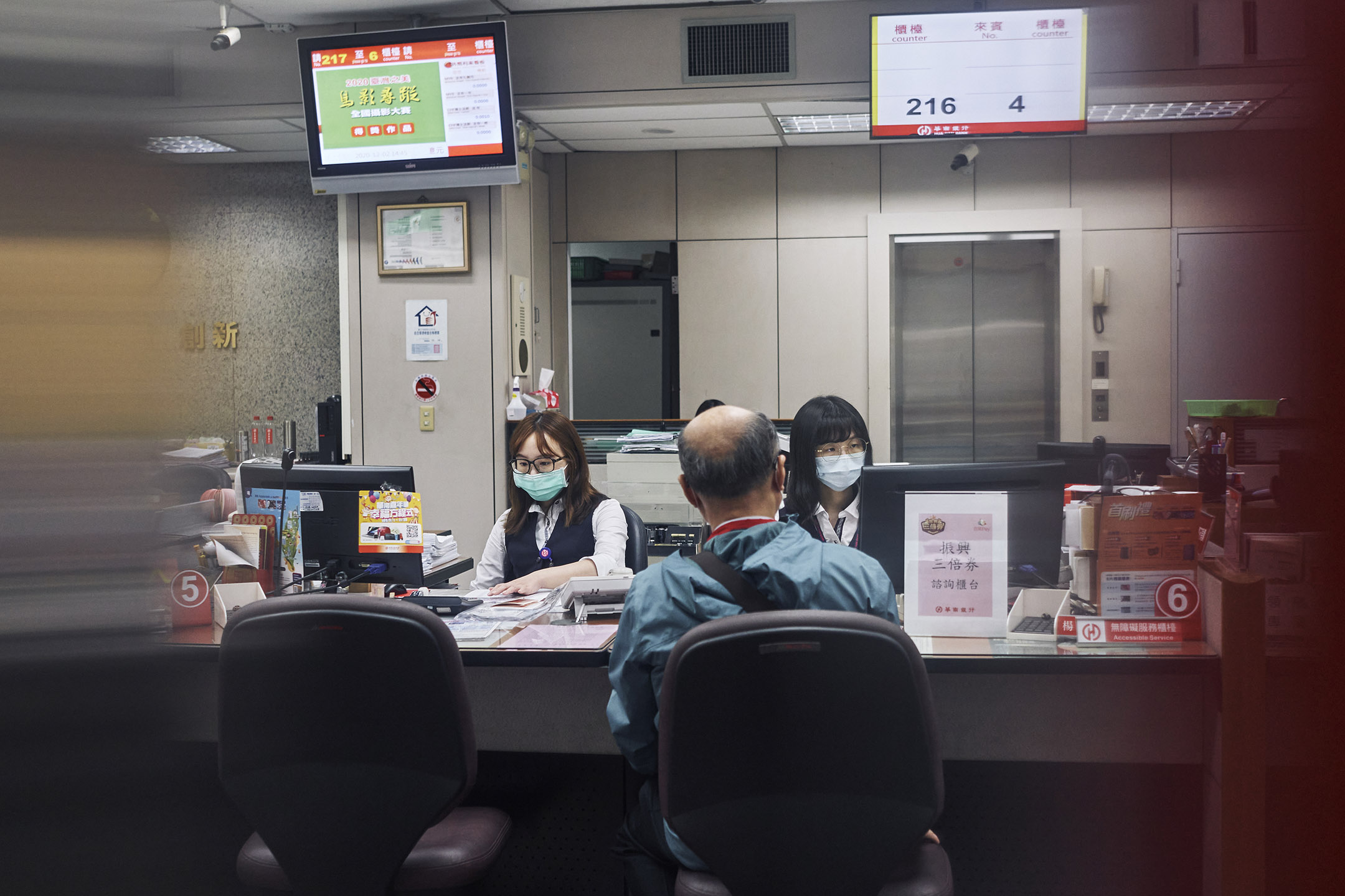 2020年12月2日台湾台北,银行柜员戴着口罩为客户提供服务。