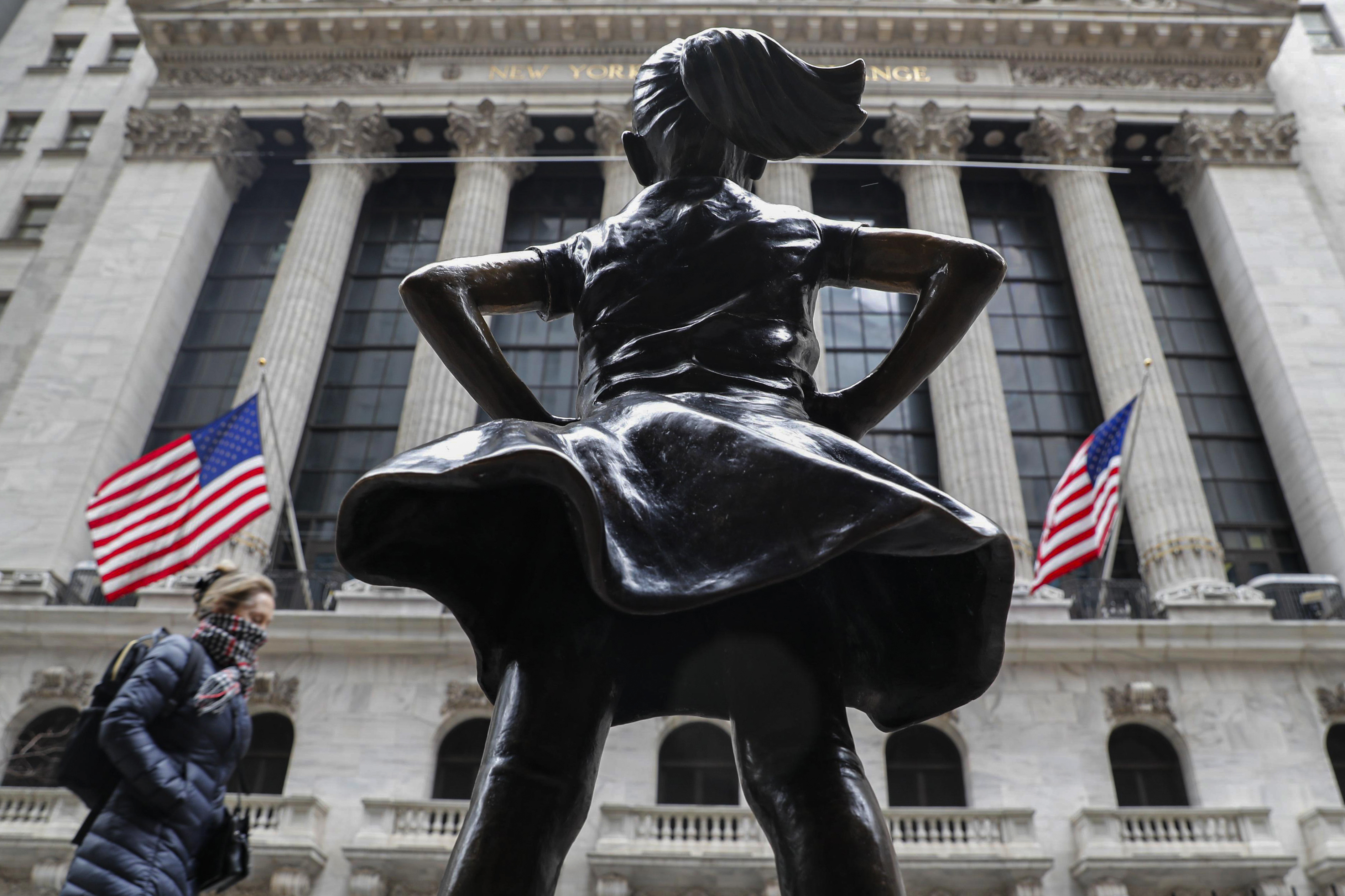 2020年3月12日纽约,一名戴着围巾的行人在纽约证券交易所 (NYSE) 和无畏女孩雕像旁散步。
