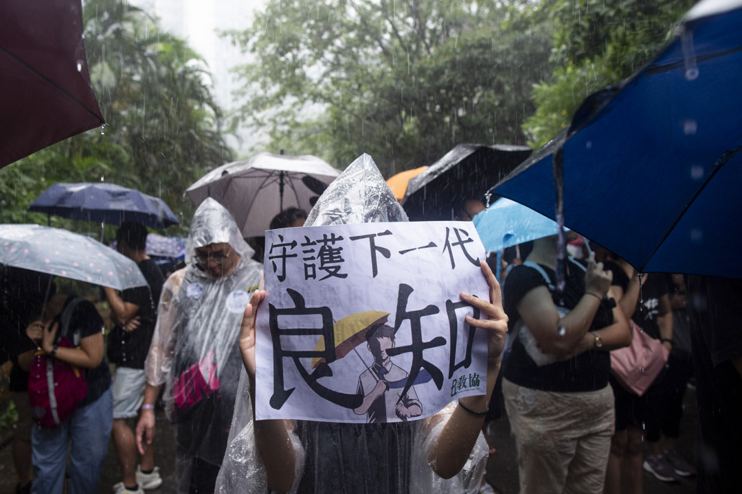 2019年8月17日,有教师发起“守护下一代,为良知发声”的游行,期间大雨滂沱,参加者身上贴上“我是香港教师”的贴纸,又手持“守护下一代良知”、“凭老师守护”的标语。 摄:林振东/端传媒
