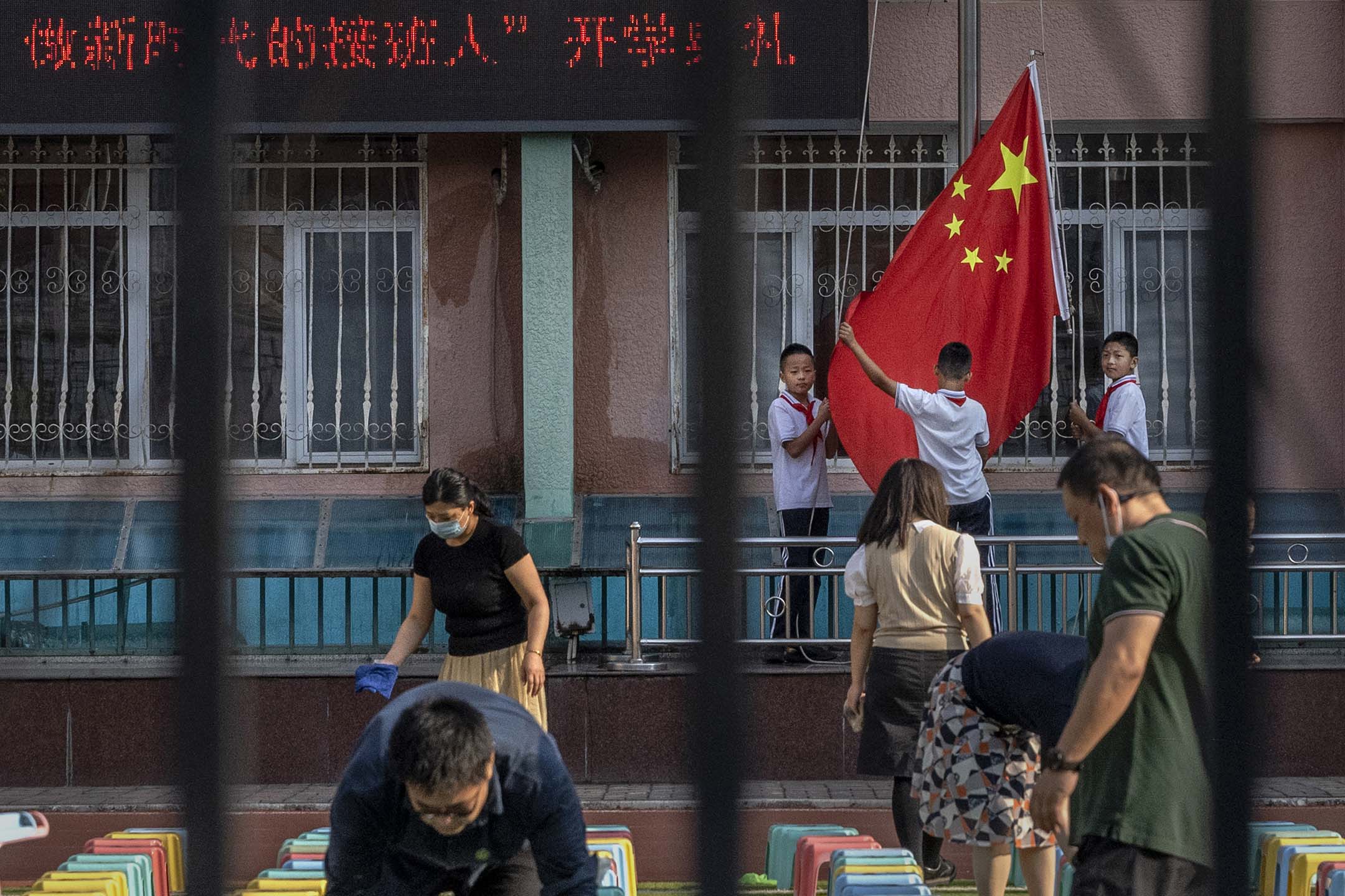 2021年9月1日中国北京,一所小学新学年第一天的开学仪式前,学生们准备一面国旗,老师们正安排凳子。