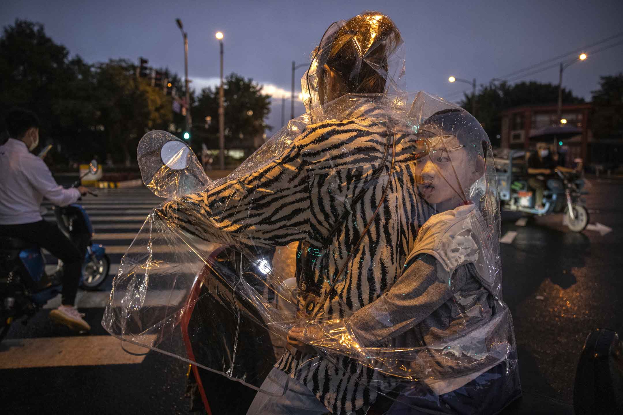 2021年9月8日,北京的一場暴雨中,一個男孩坐在他母親的塑料雨衣裡,等待紅綠燈過馬路。