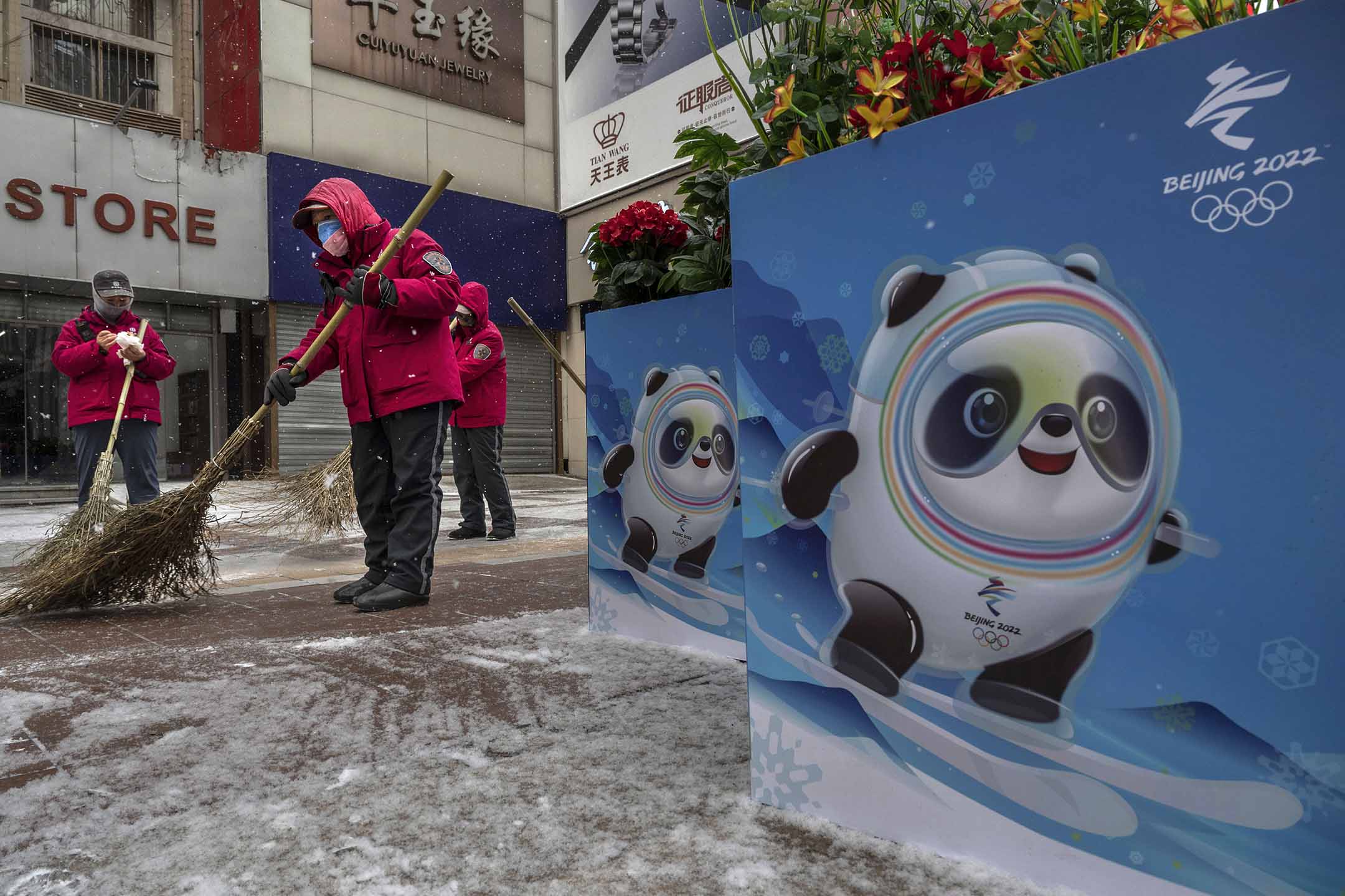 2022年1月20日北京,志願者在北京冬奧會和殘奧會海報旁邊掃雪,海報展示了吉祥物「冰墩墩」。