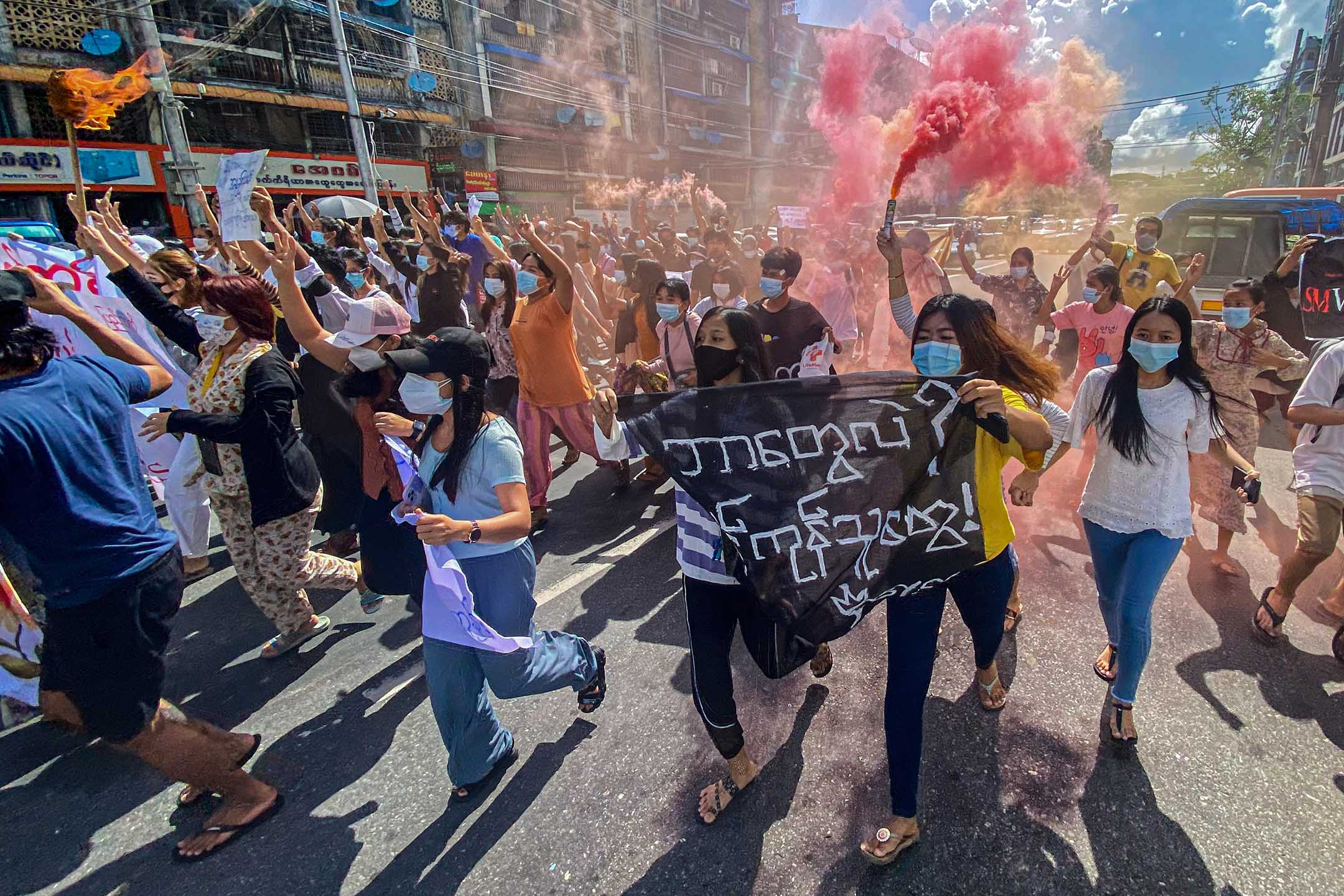 2021年7月14日缅甸仰光,仰光举行的反政变示威的游行中,妇女手持横幅和紧急信号棒。