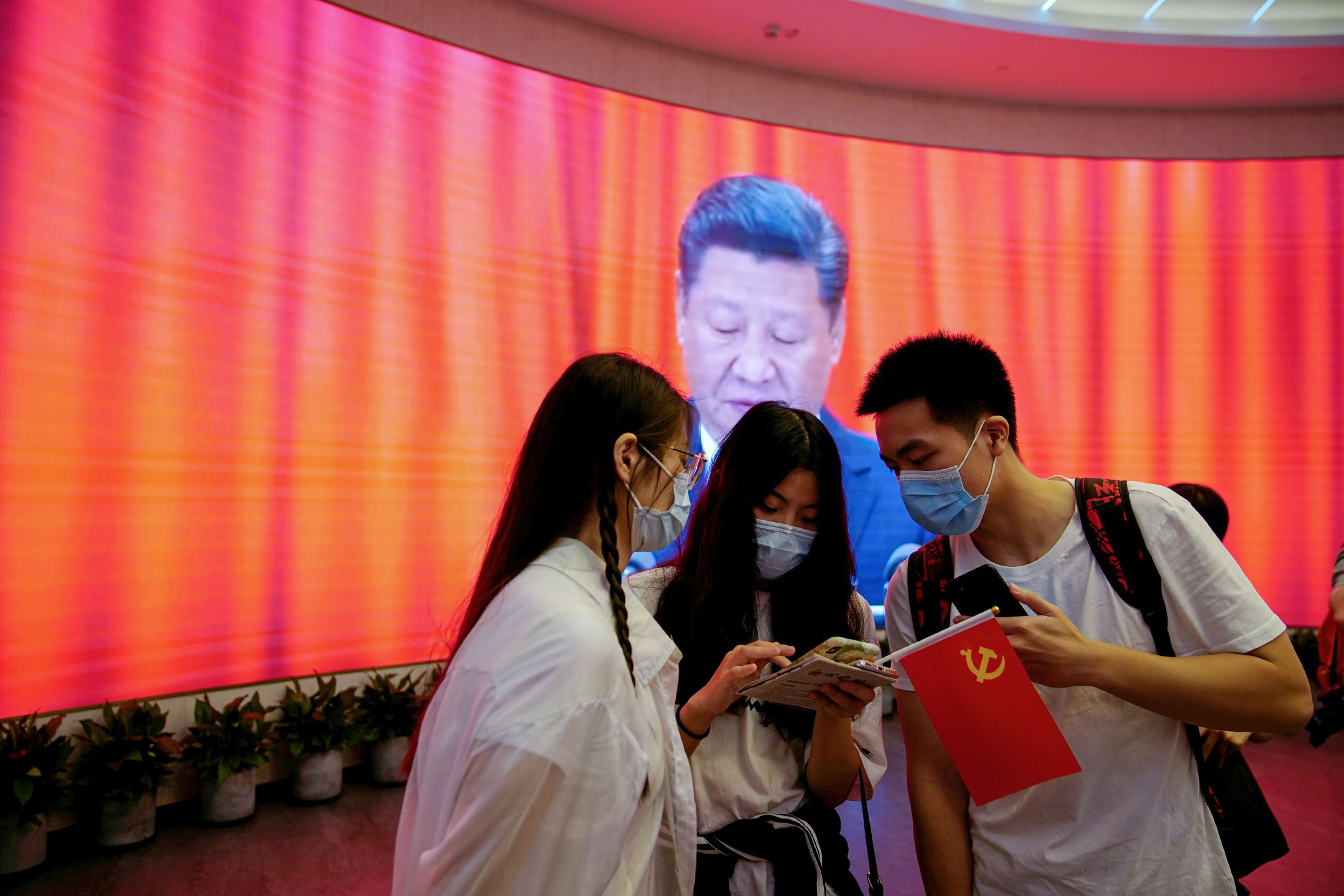 2021年6月4日,中国上海,纪念中国共产党成立100周年活动中,一名妇女在显示中国国家主席习近平的屏幕前看手机 .