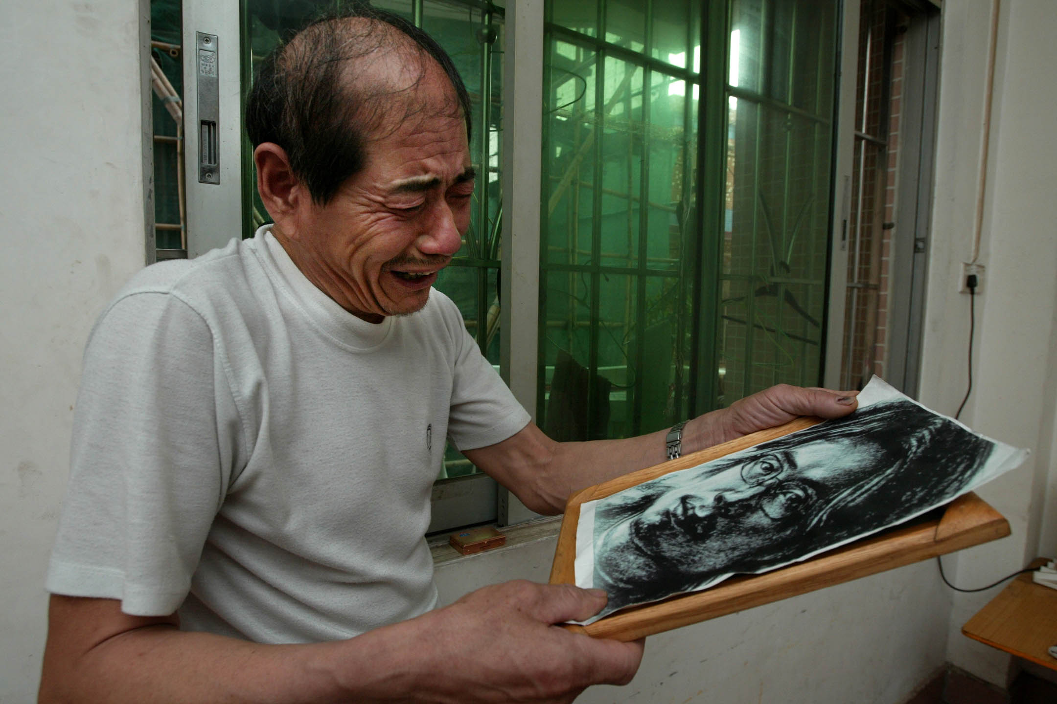 2003年4月29日,孙志刚因无担保文件被广州拘留,后在看守所中死亡,孙志刚父亲在广州租住的家里拿著儿子的画像。