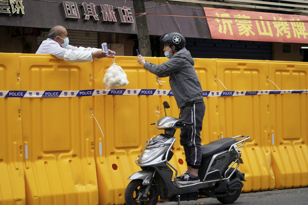 2022年3月30日,中國上海,一名站在機車上的男子越過封鎖區路障掃描二維碼,向商販購買食物。