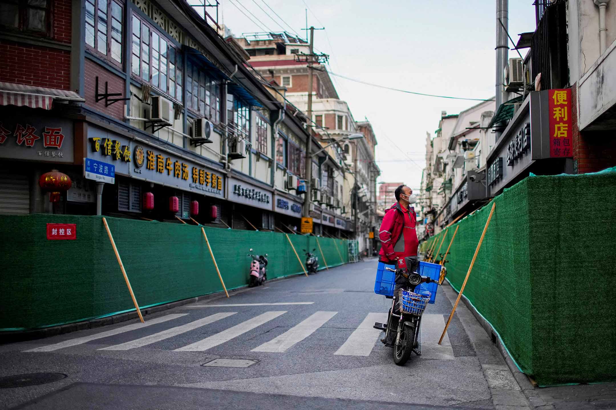 2022年5月9日,上海,疫情期间,一名站在机车上的送货员在封锁的住宅区探看。