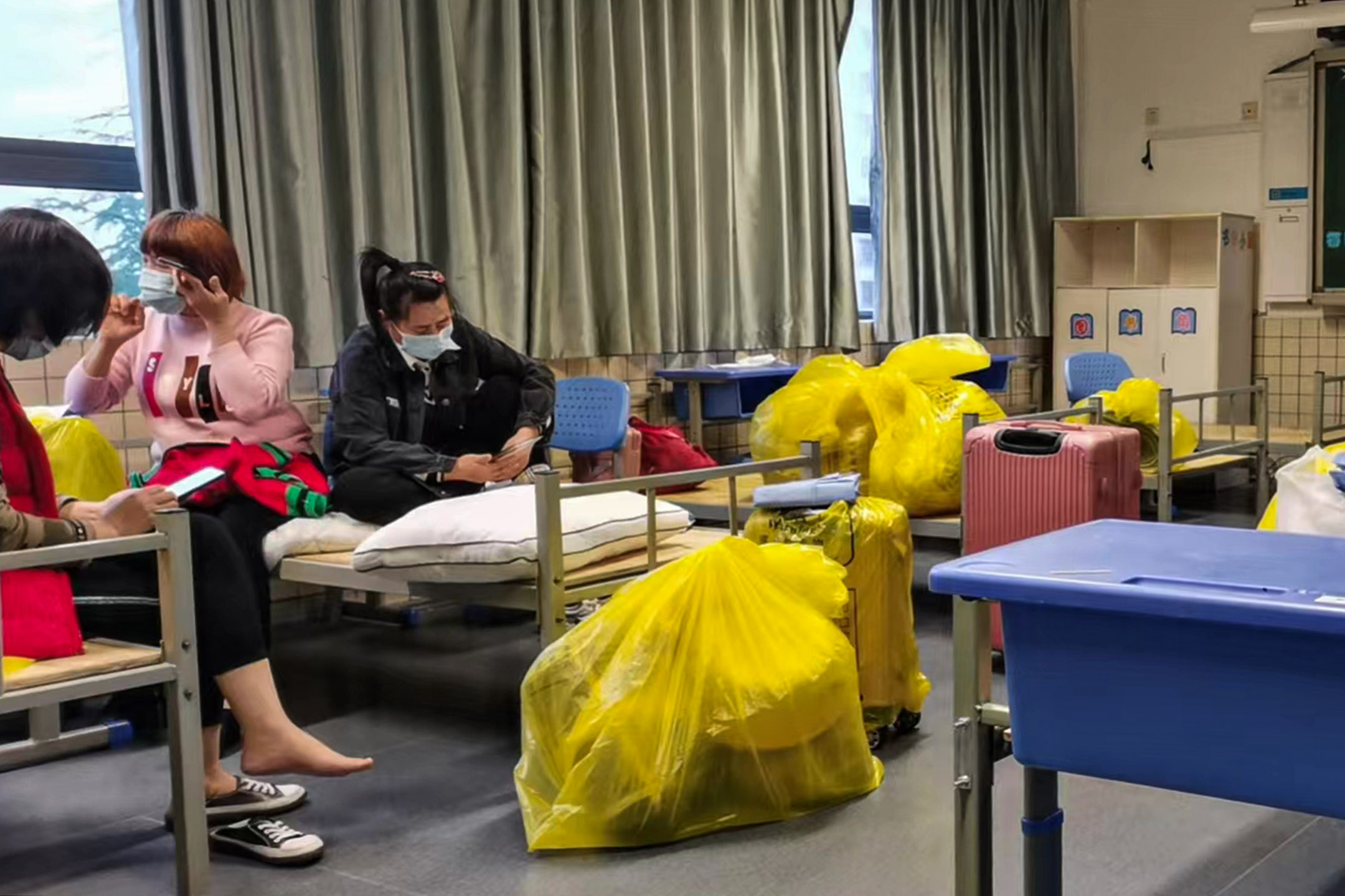 五月初,上海某小學教室內,眾人將被子和床墊裝進黃色醫用垃圾袋,等待大巴接送轉運到另一個收容站。