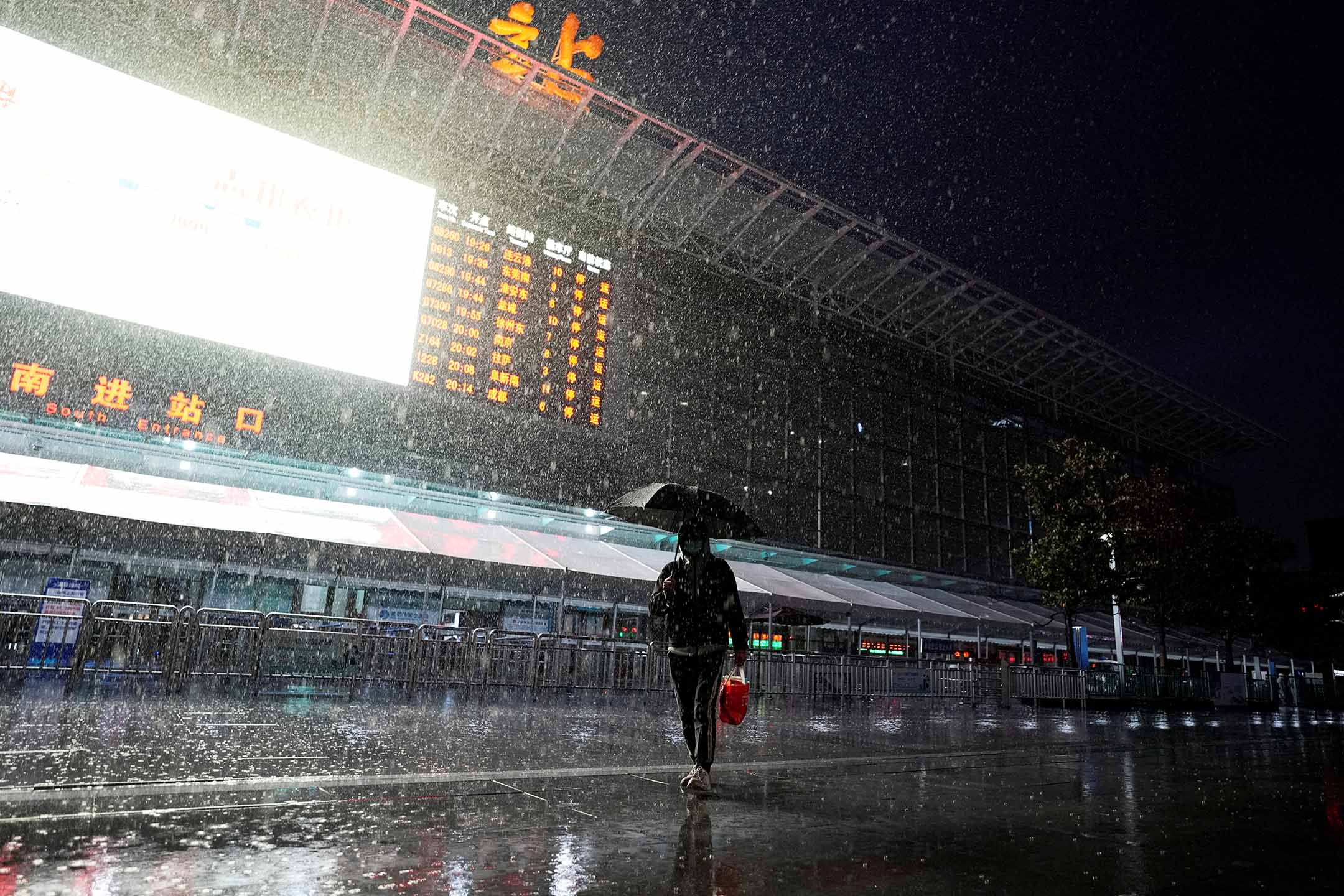 2022年3月21日,上海,一名戴著口罩的男子冒雨走過上海火車站。