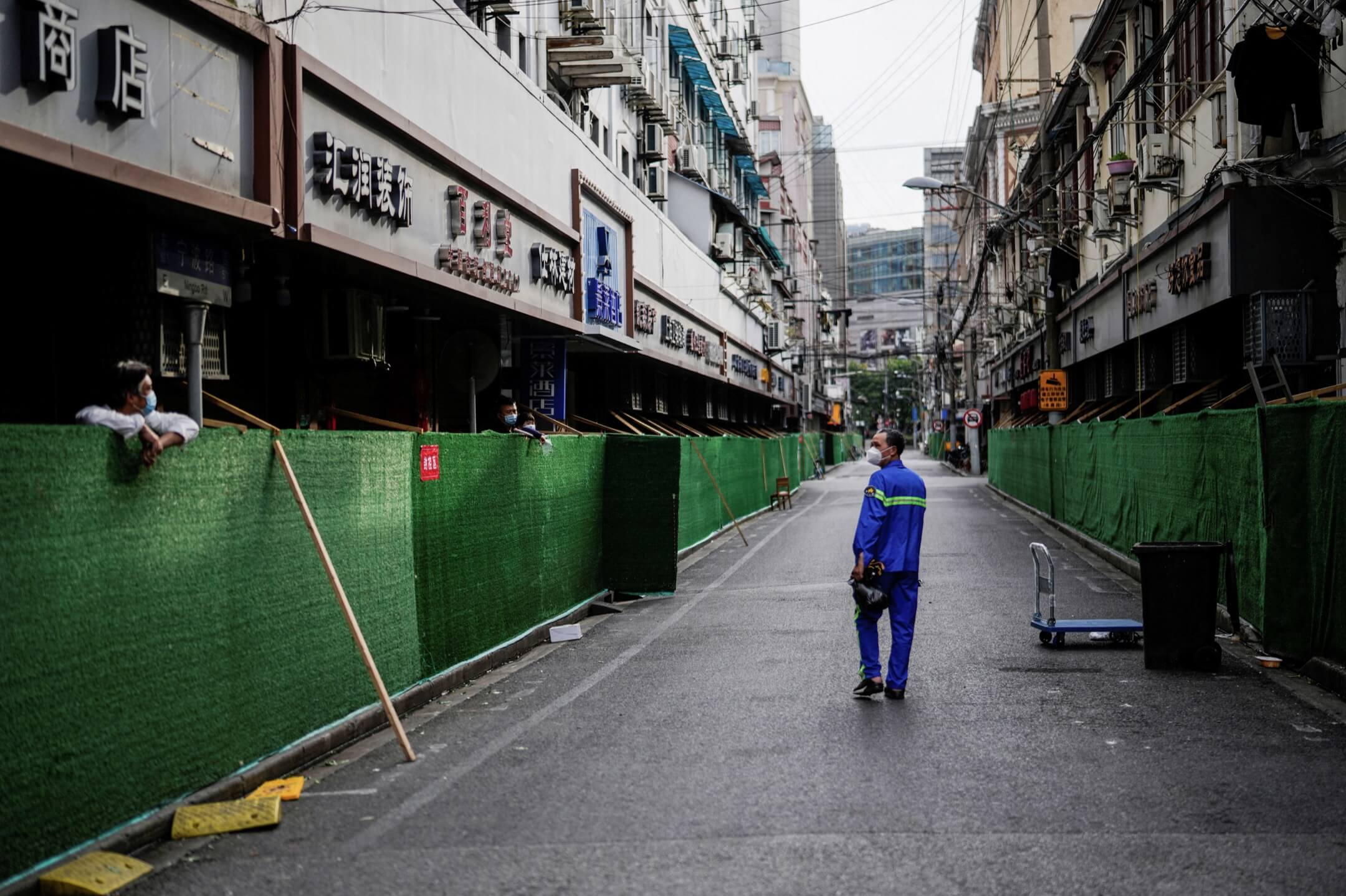 2022年5月18日,中国上海,一名清洁工人在围封的住宅区间走过,与被围封的居民对望。