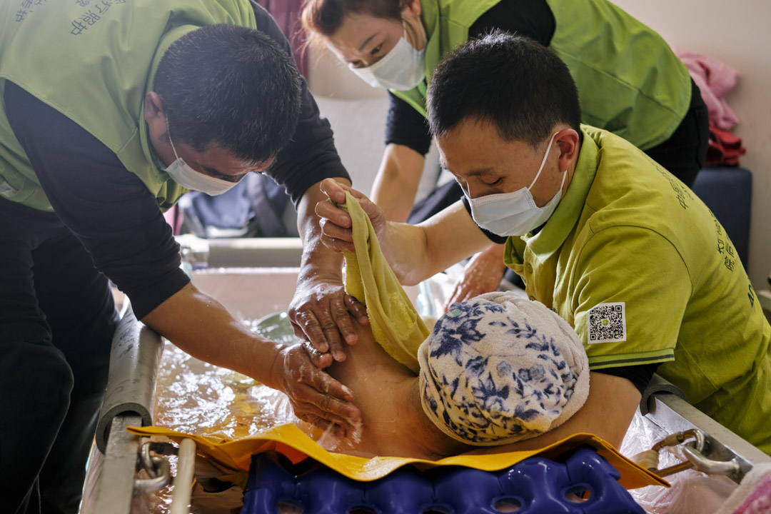 老人翻身洗背时需要两个助浴师一起,陈菊清侧卧在助浴师手臂上。
