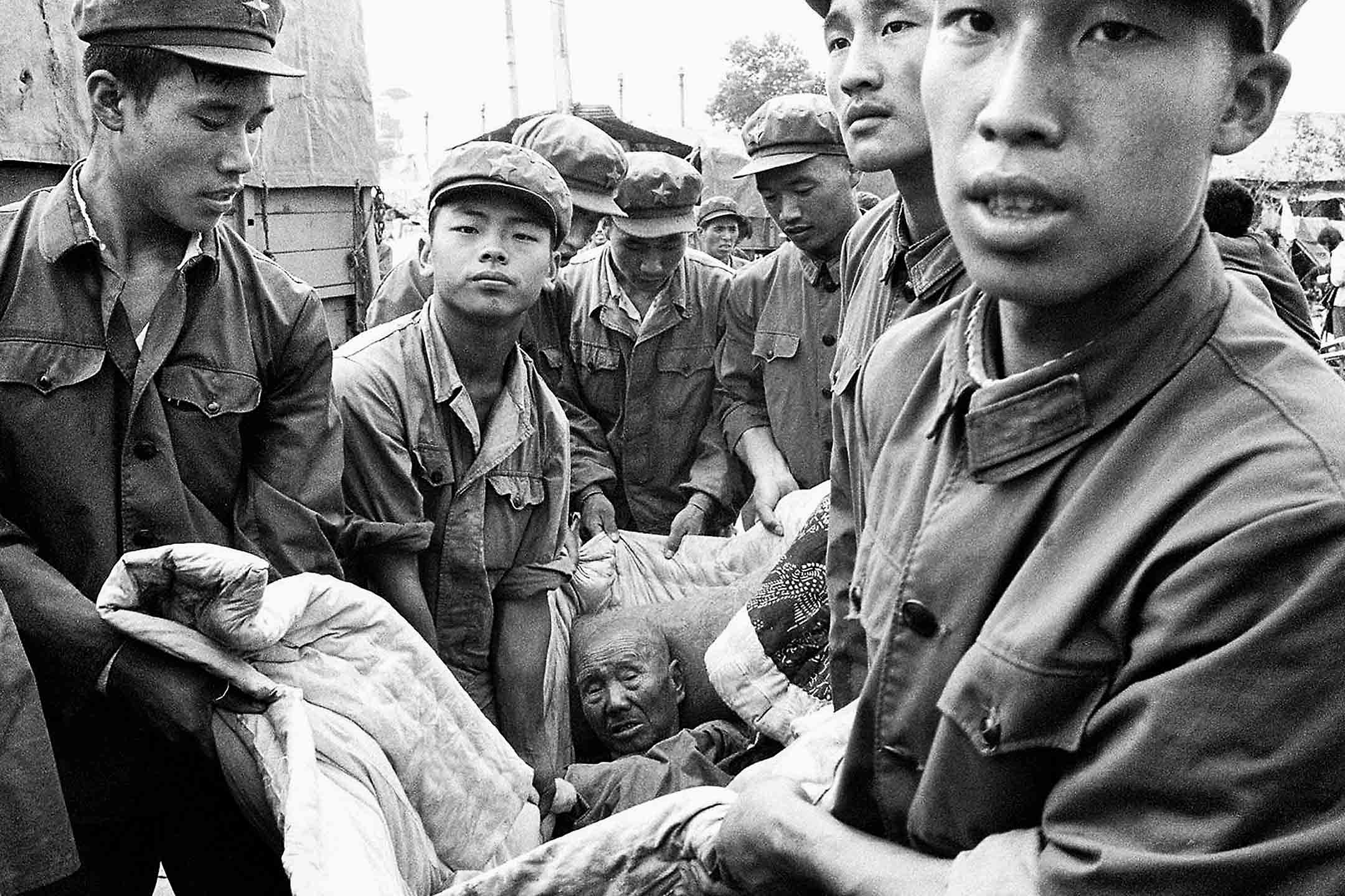 1976年7月28日,唐山大地震后,解放军将一名受伤的年长男子抱在被子里。