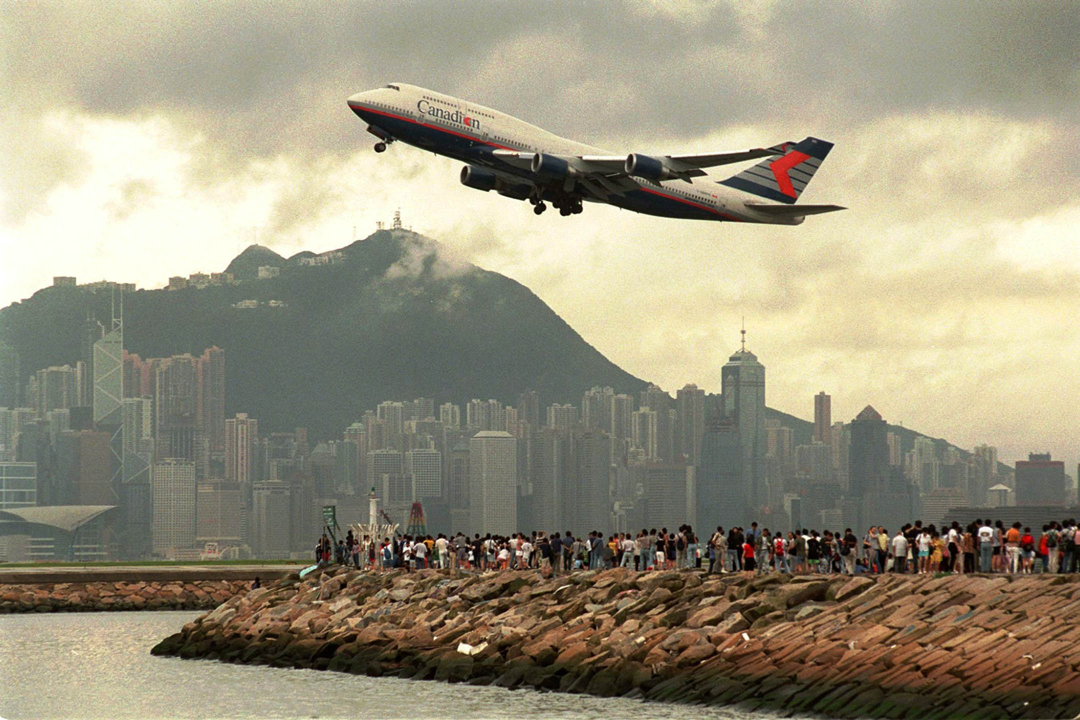1998年7月5日,香港啟德機場跑道旁邊的海港,大批人群聚集在海堤上,觀看最後一架飛機離開機場。