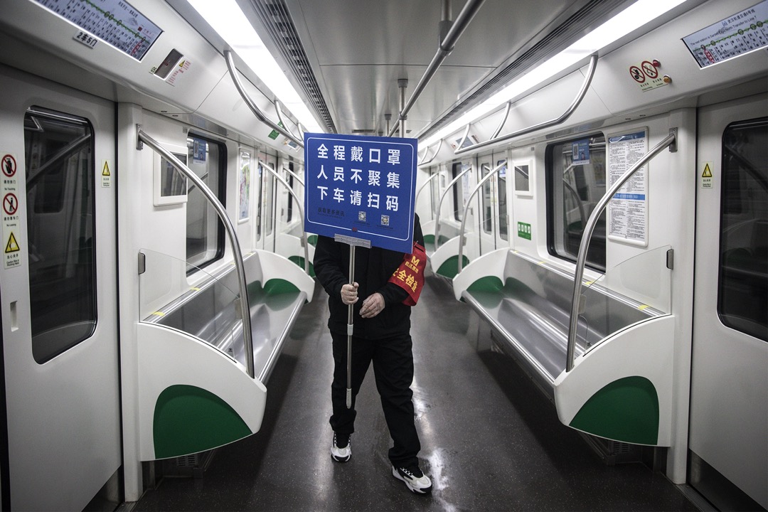 2020年3月,中国武汉,一名工作人员在没有人的地铁车厢内举起告示牌提醒乘客要时刻配戴口罩。