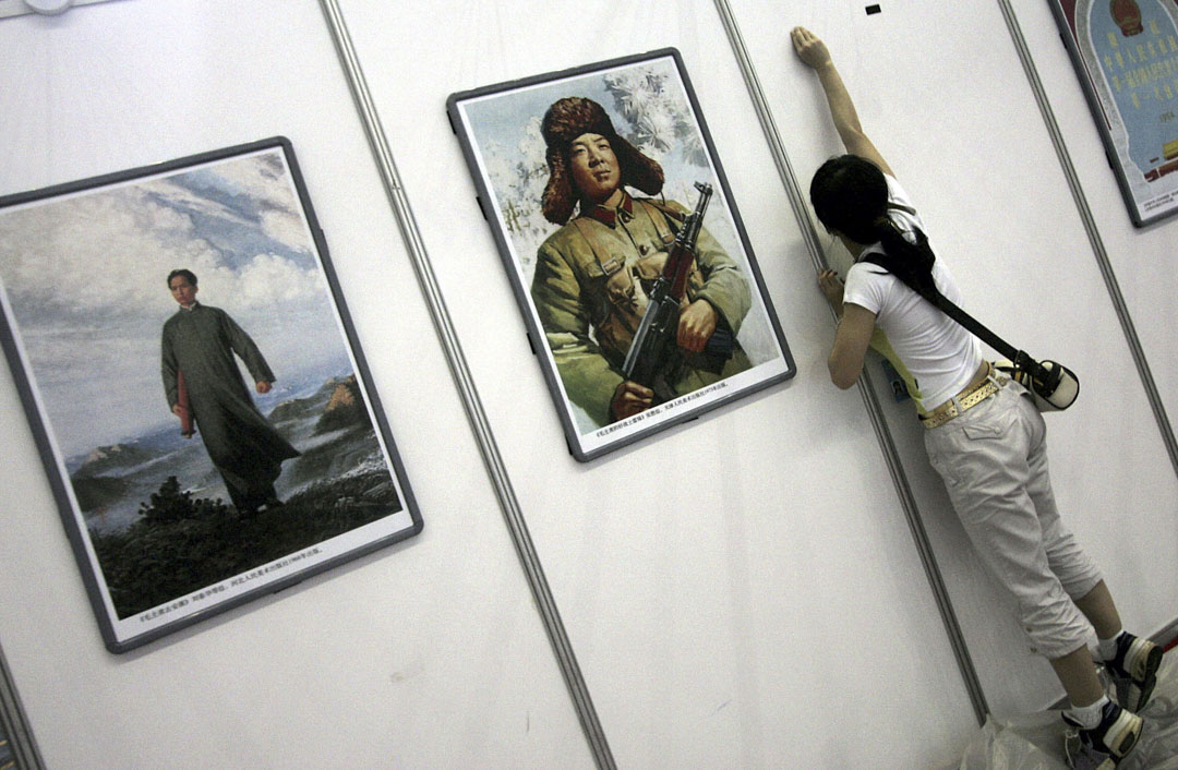 2006年深圳国际文化产业博览会上,一名工人在展览区布展,当中有雷锋及已故领导人毛泽东的海报。