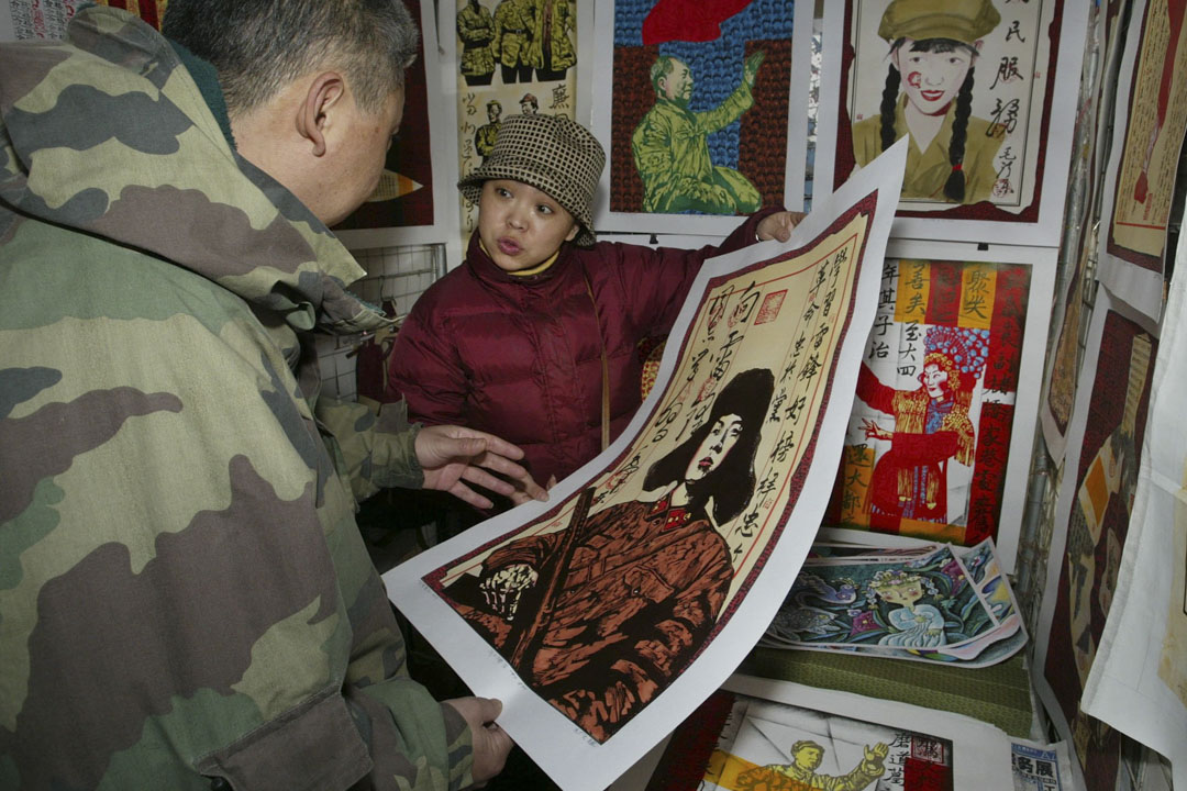 2002年11月10日,北京的潘家园市场的一位现代艺术品经销商,向顾客展示了一幅共产党偶像雷锋的画作。