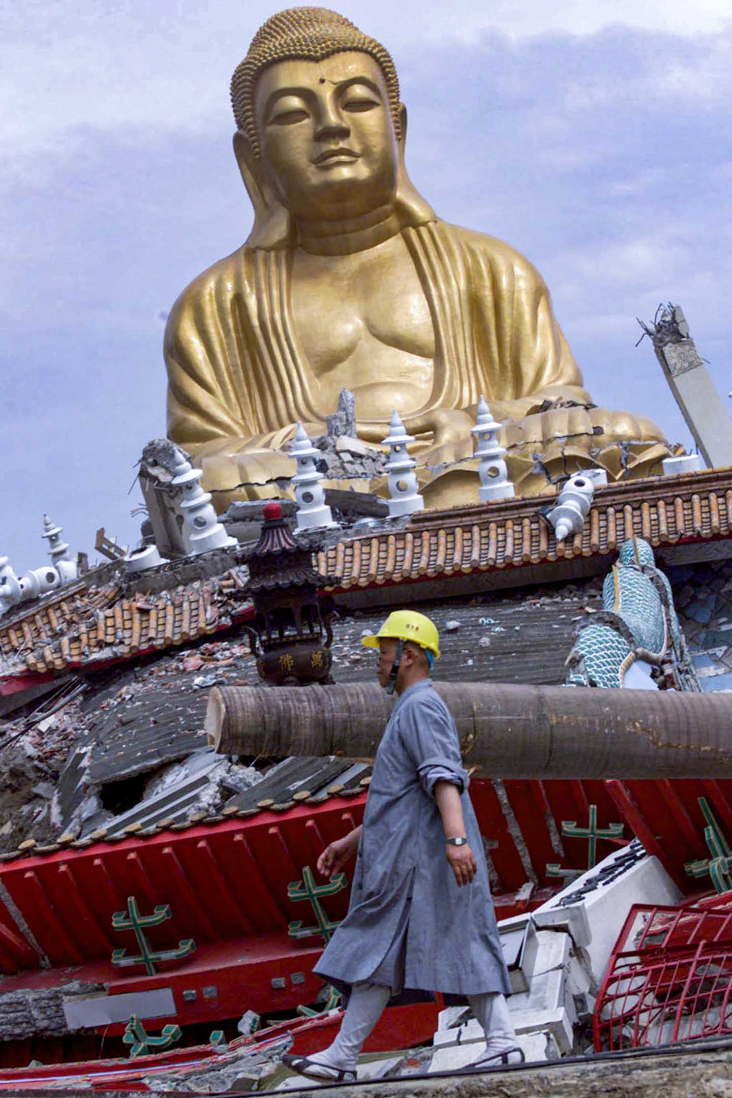 1999年9月26日,台灣南投一座寺廟的尼姑路過地震後受損的佛像。