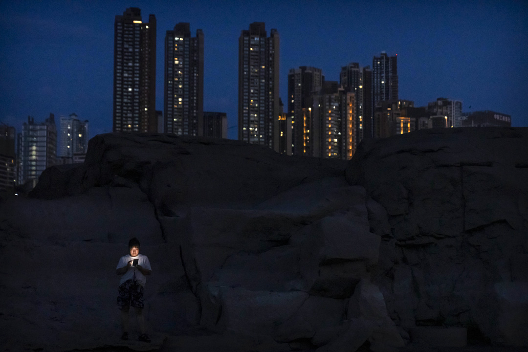 2022年8月19日,重慶市,一名婦女站在長江旁的岩石上看手機。