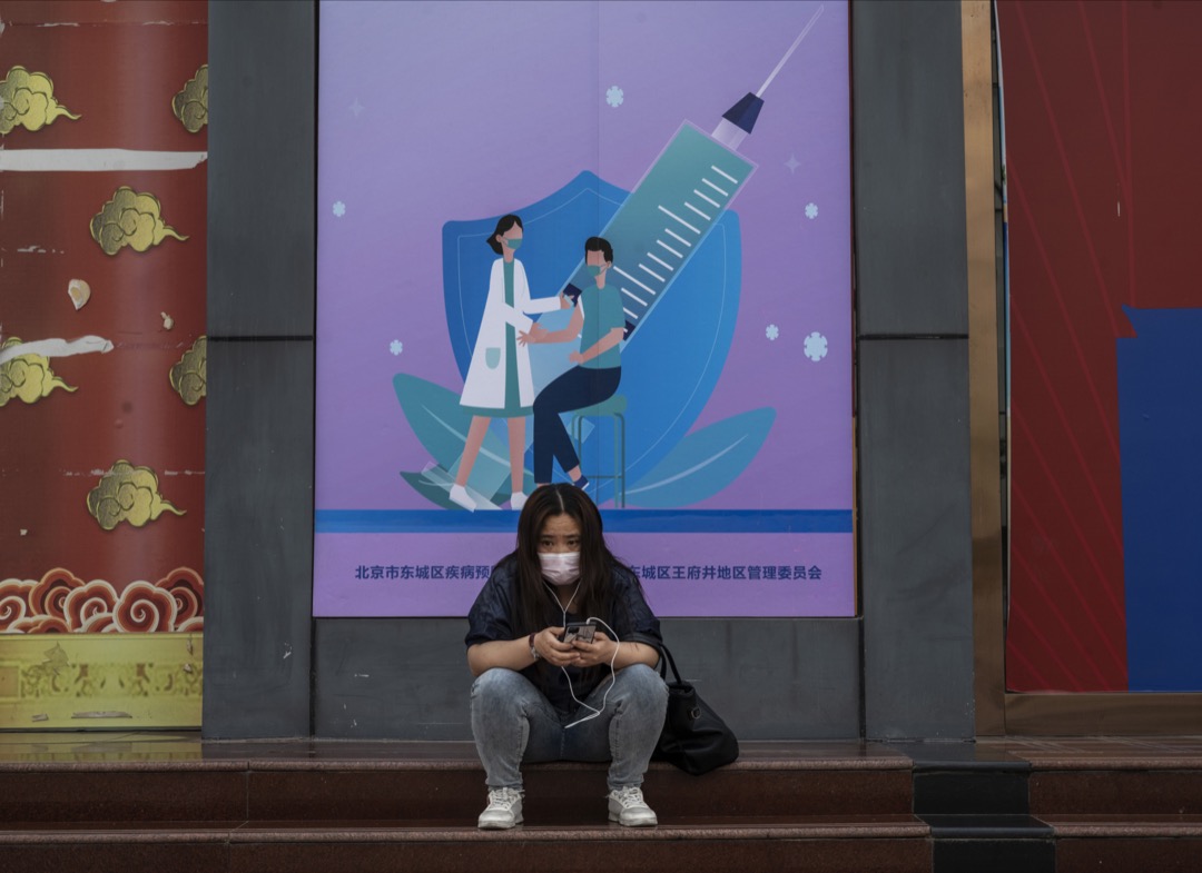 2021年5月23日,中国北京,一名女子坐在一个推广疫苗接种的广告版前。