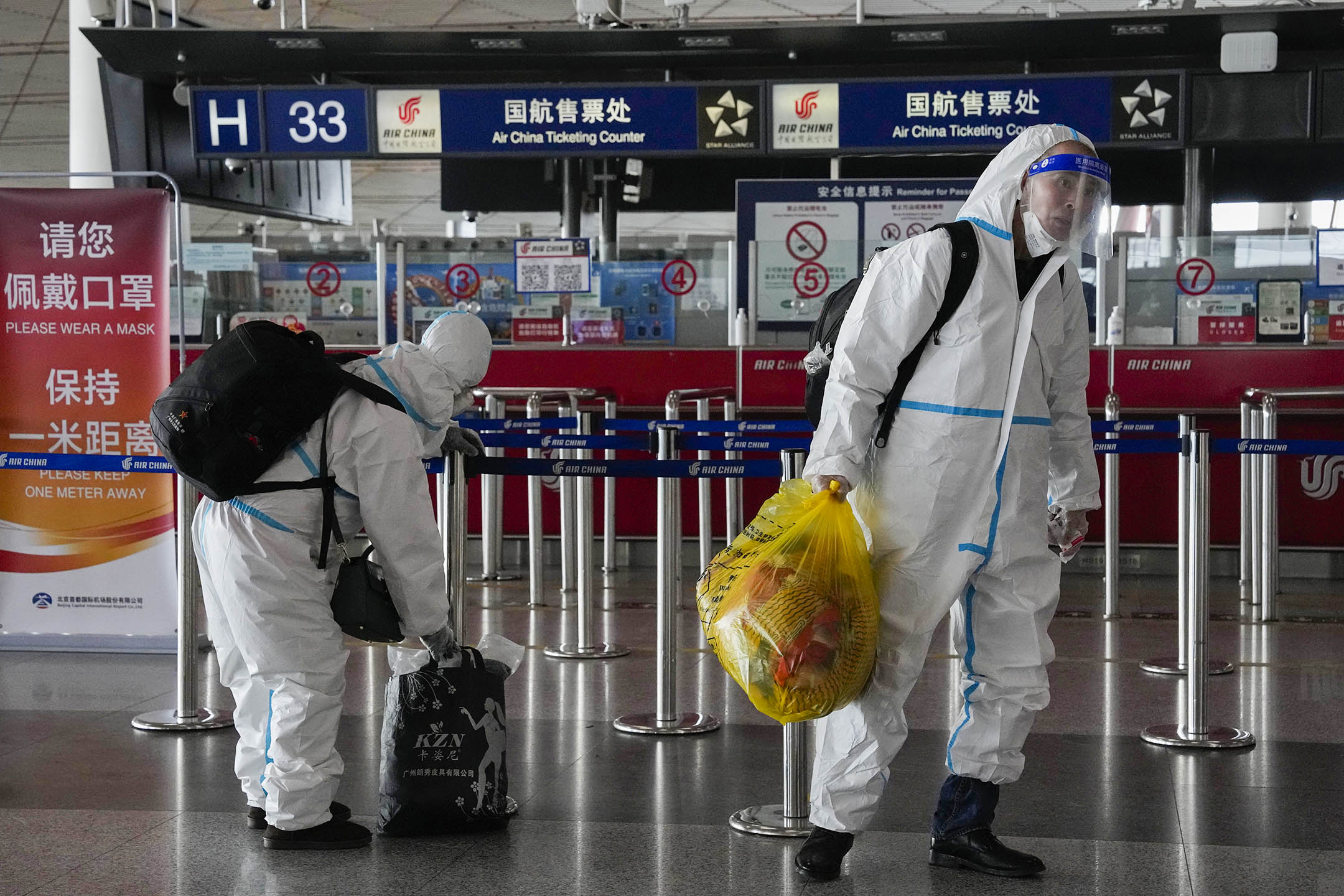 2022年12月13日,北京首都國際機場,穿著防護衣的乘客拿著行李。