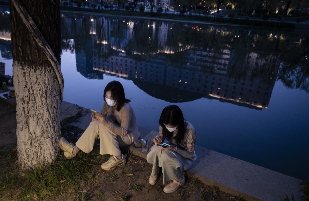 2022年5月2日,中国北京,两名女子坐在亮马河畔用手机。