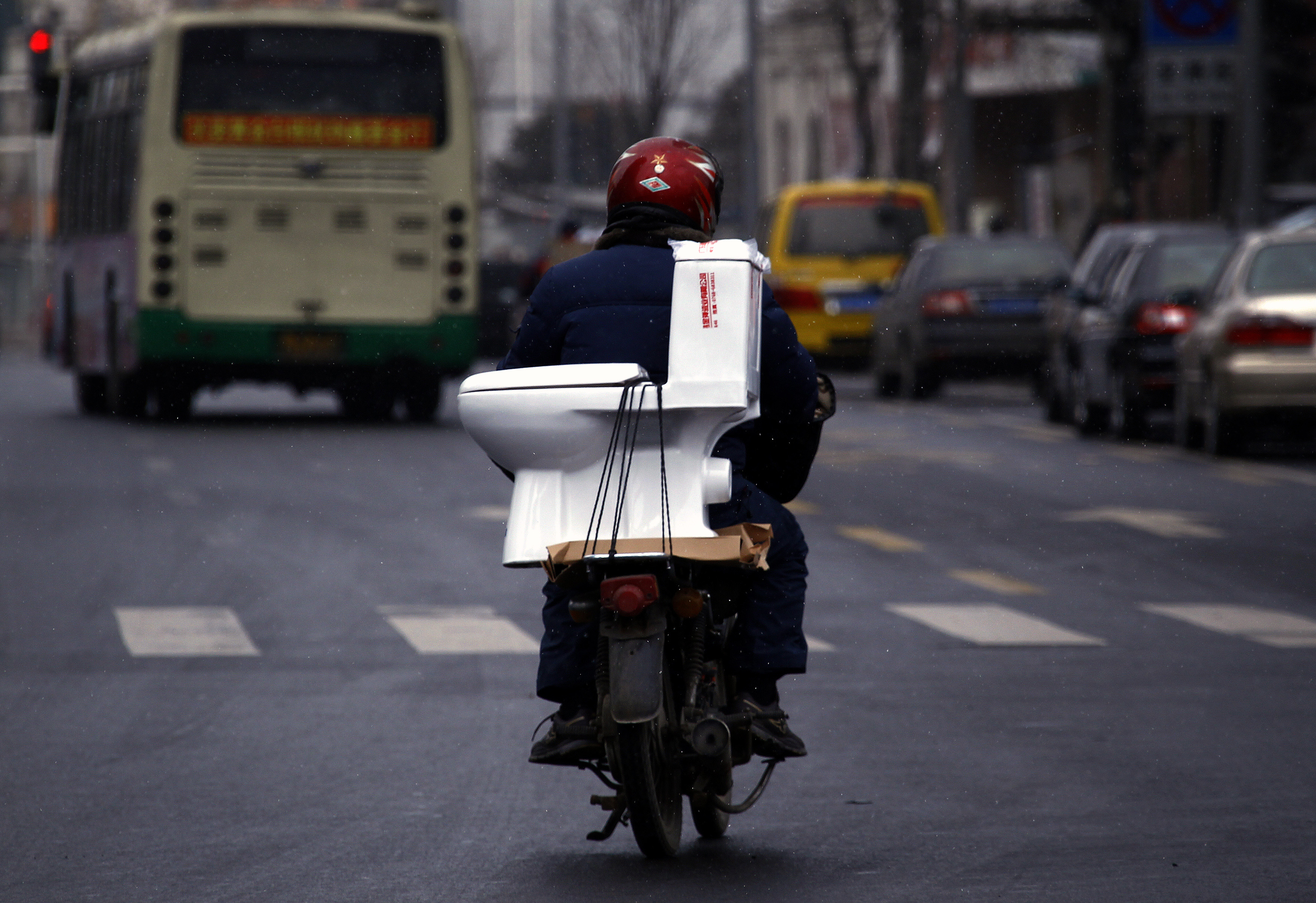 2012年2月7日,山東省煙台市,一名男子在街道上騎著一輛摩托車,一個馬桶綁在座椅後部。