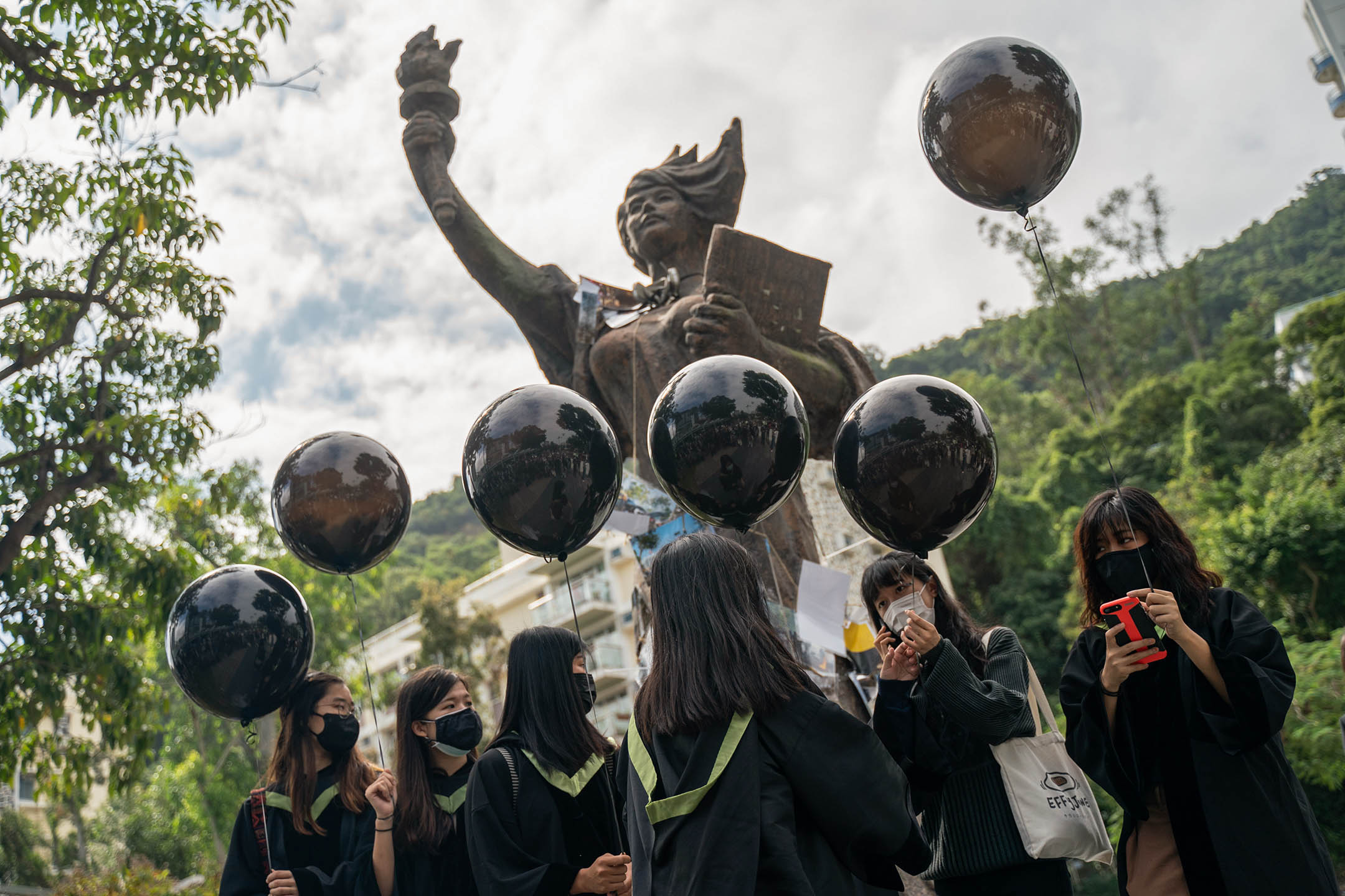 2020年11月19日,香港中文大学,身著黑色毕业袍和口罩的学生站在民主女神像前,举著黑色气球。
