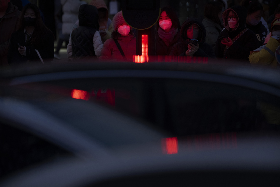 2023年2月15日,戴著口罩的女子在北京等紅燈穿過十字路口。