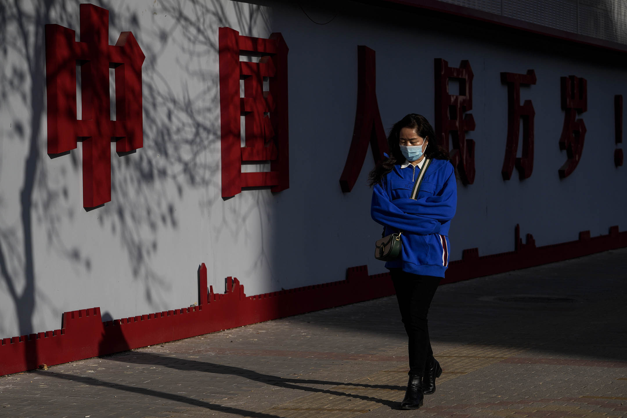 2023年3月2日,北京,戴着口罩的女士走过一幅写着“中国万岁”字样的墙。摄:Andy Wong/AP/达志影像