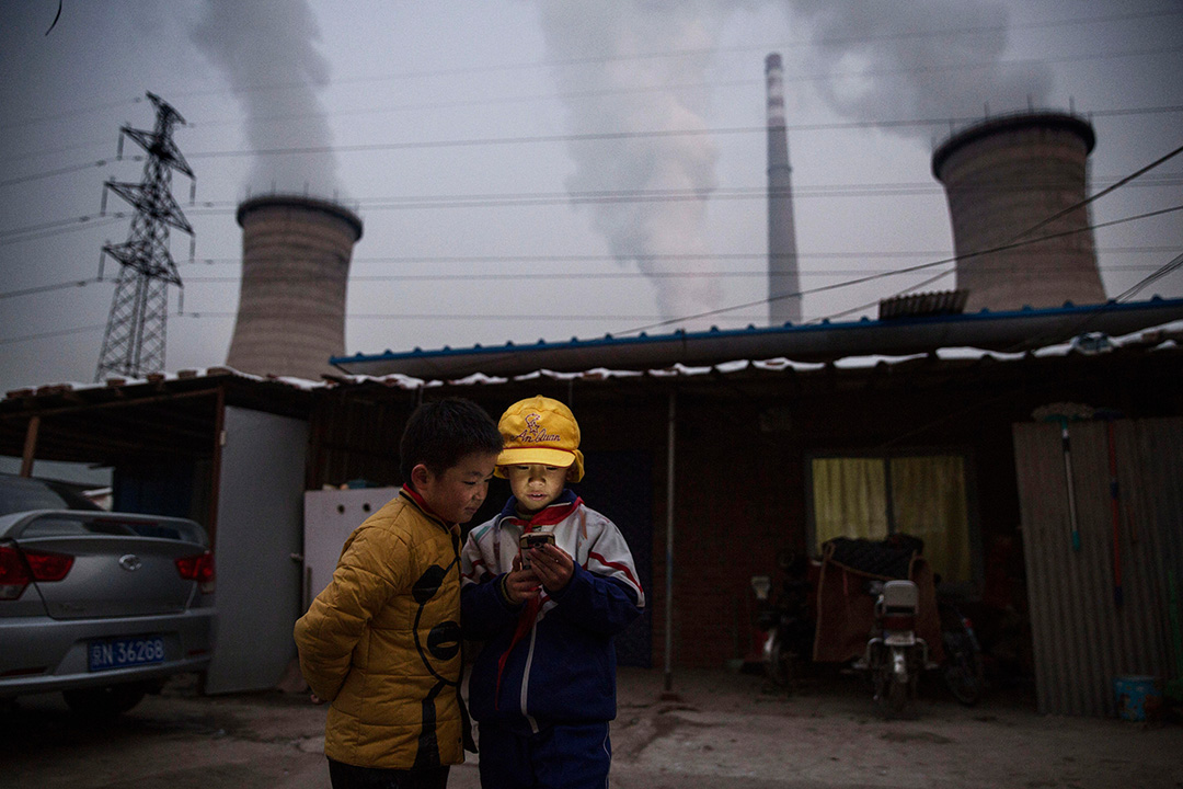 2015年11月27日， 中國北京，一對男孩在燃煤發電廠前使用智能手機。攝：Kevin Frayer/Getty Images