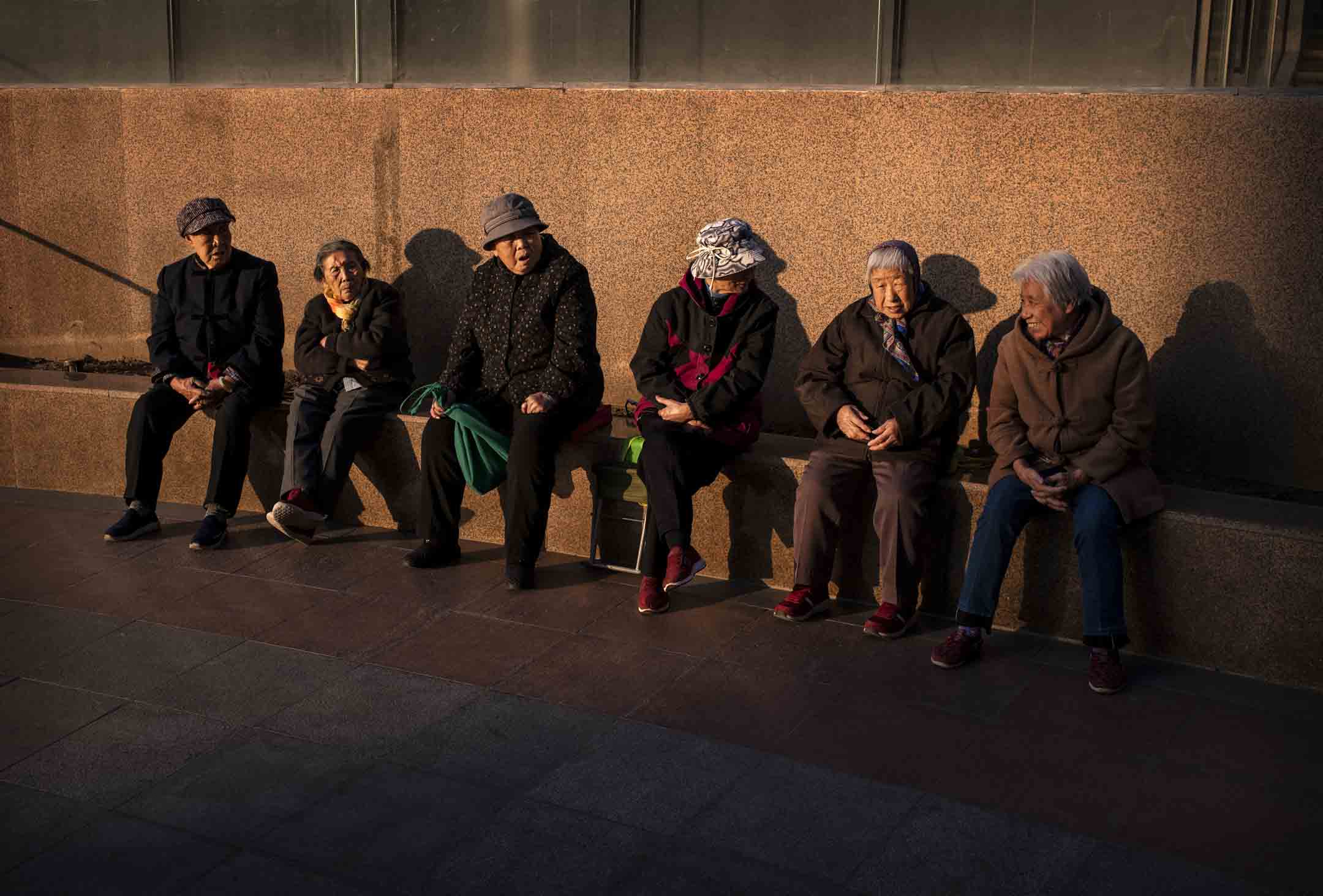 2019年11月8日,中国北京的一家购物中心外,长者在夕阳下聊天。摄:Kevin Frayer/Getty Images