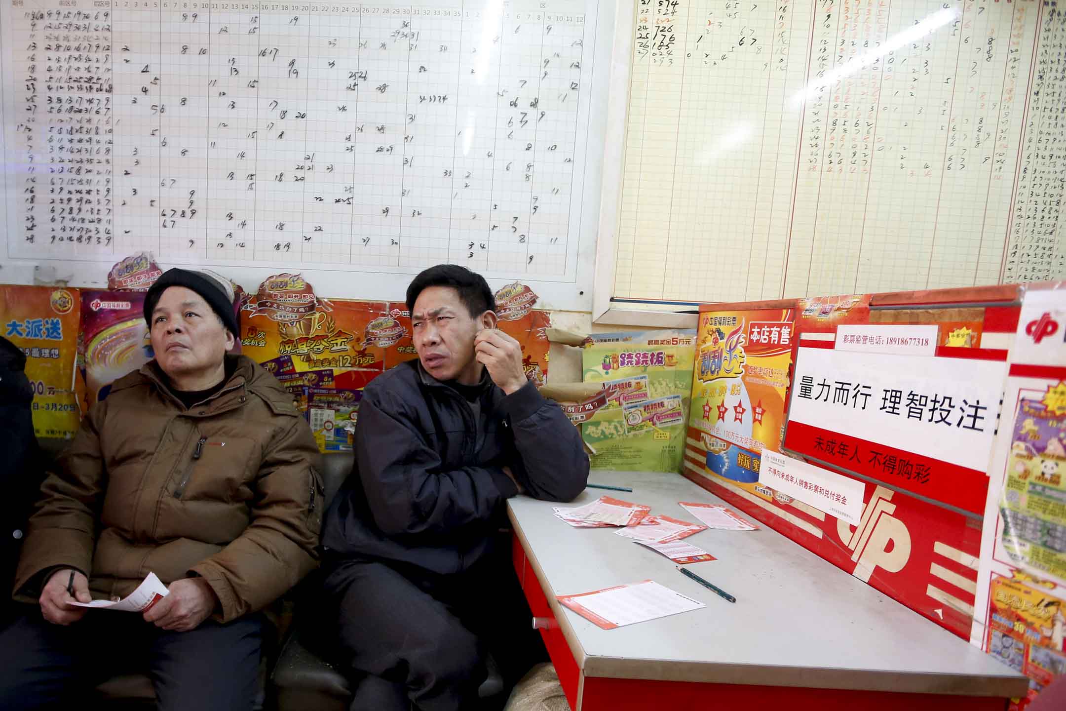 在刮刮樂投注站內,市民手拿著彩票,看著一旁的電視機。攝:Aly Song/Reuters/達志影像