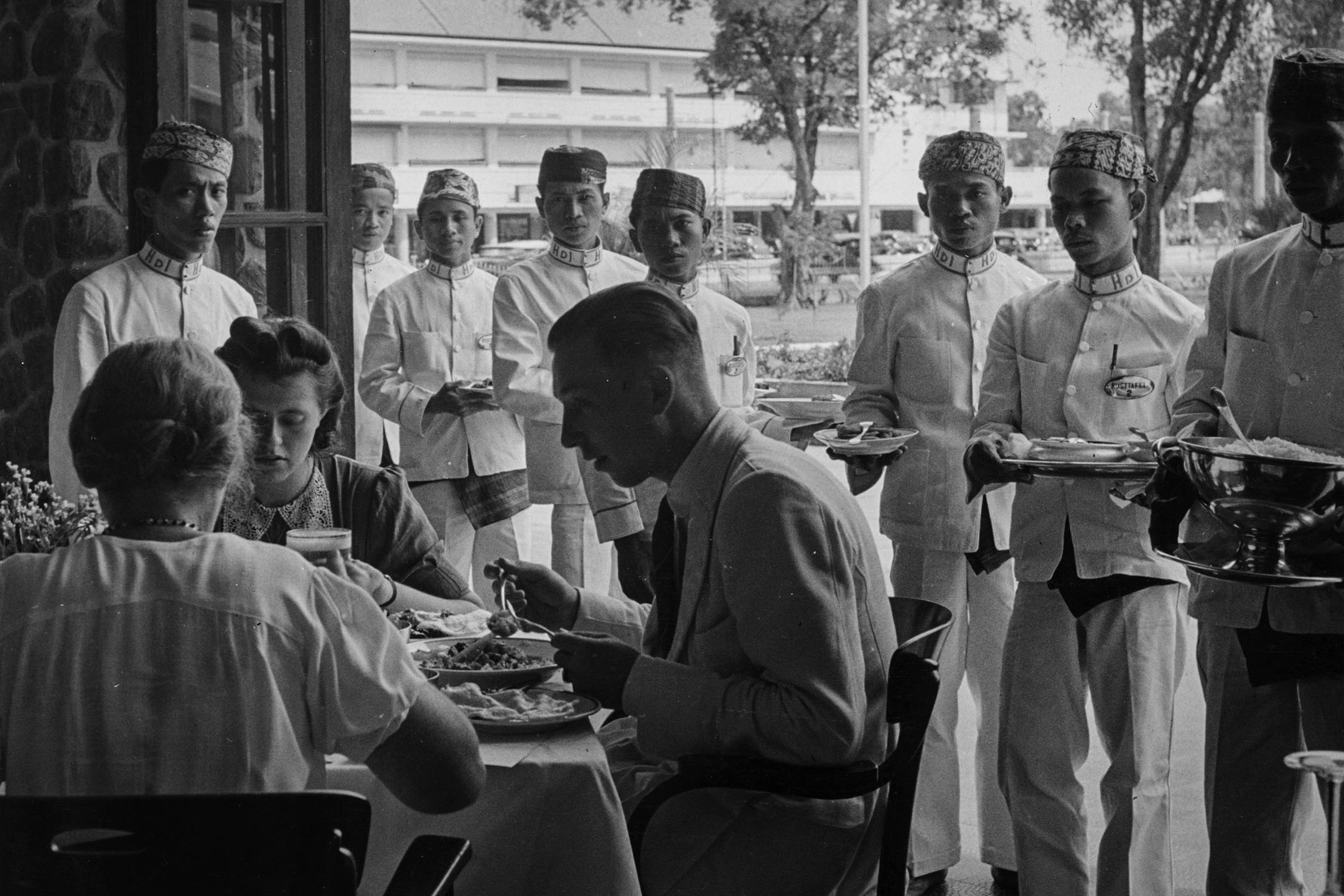 1940年，荷兰殖民者在印尼爪哇吃饭，一群服务员在场。摄：Three Lions/Getty Images
