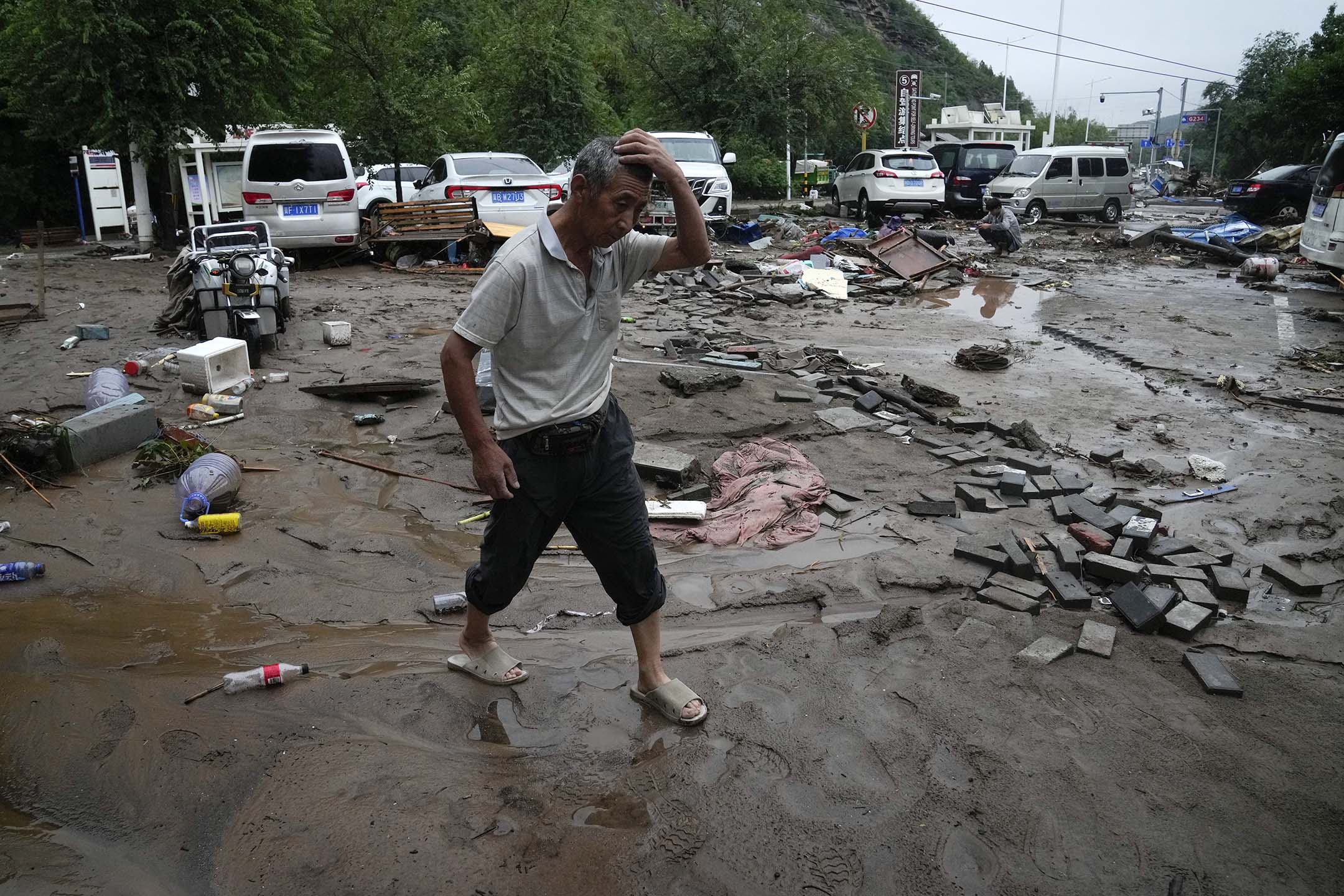 2023年7月31日,北京,连续降雨引发警报,一名男子走过被洪水损坏的车辆和道路。摄:Andy Wong/AP/达志影像