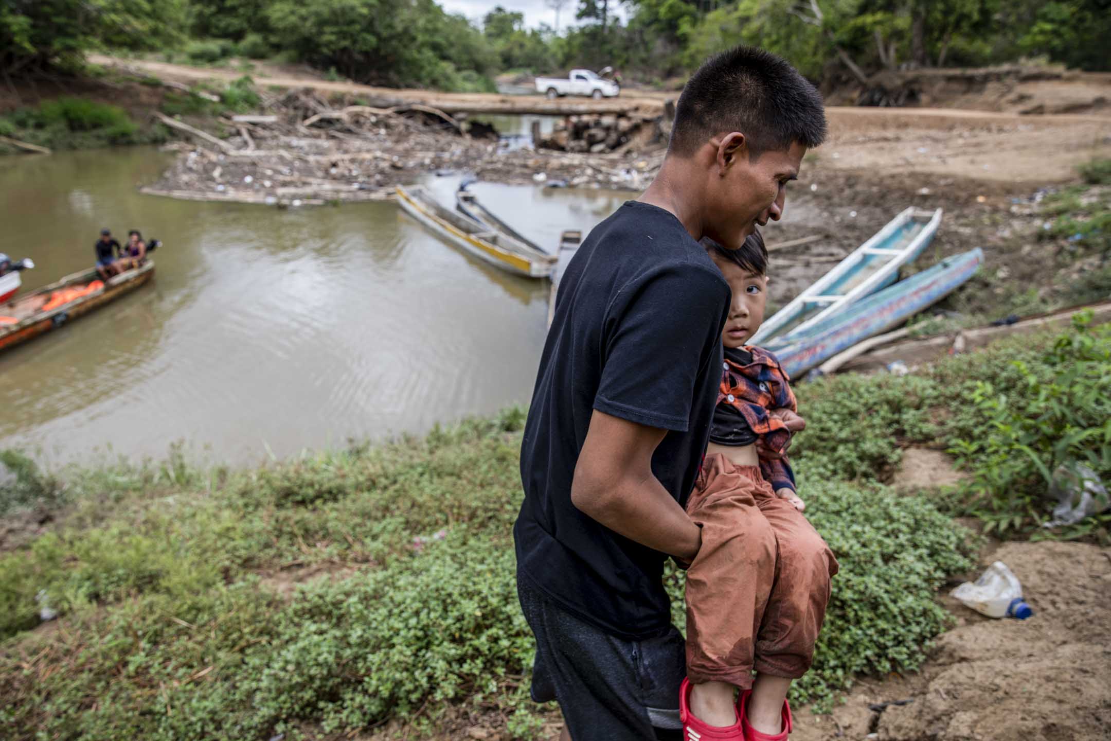 一個6歲孩子和父親在雨林艱苦跋涉四天後,乘船到達達連隘口的出口處,當地人把他抱出竹筏。攝:Shawn Yuan/端傳媒