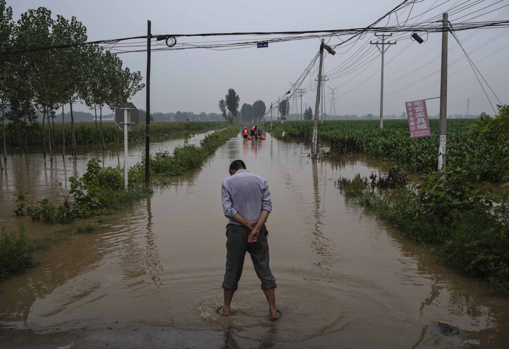 2023年8月3日,中国河北省涿州附近的一个被洪水淹没的地区,一名当地居民等待救援人员船只。摄:Kevin Frayer/Getty Images