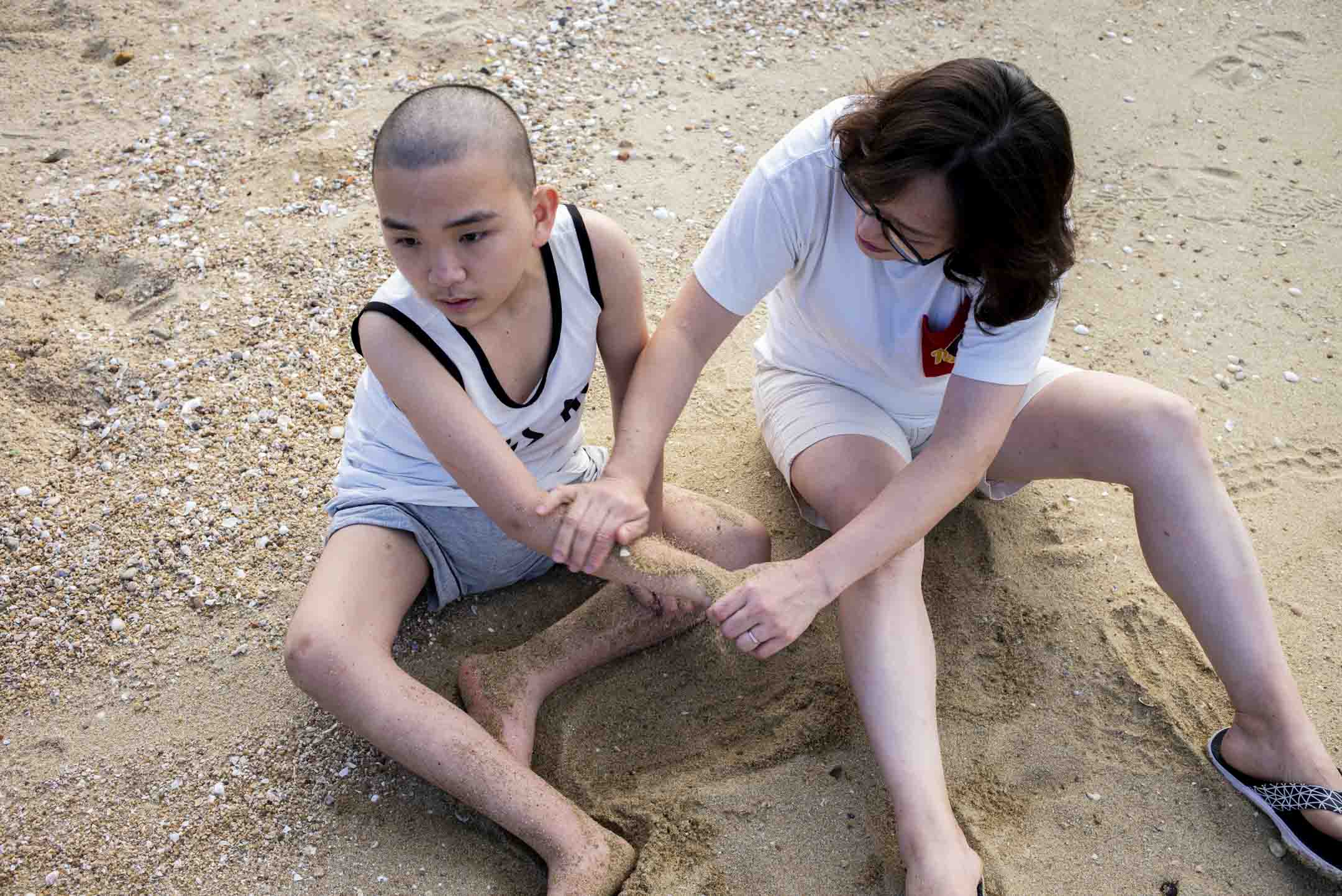 家明與媽媽坐在沙灘,媽媽把沙子放在家明的手上,讓他感覺到沙子的觸感。攝:林振東/端傳媒