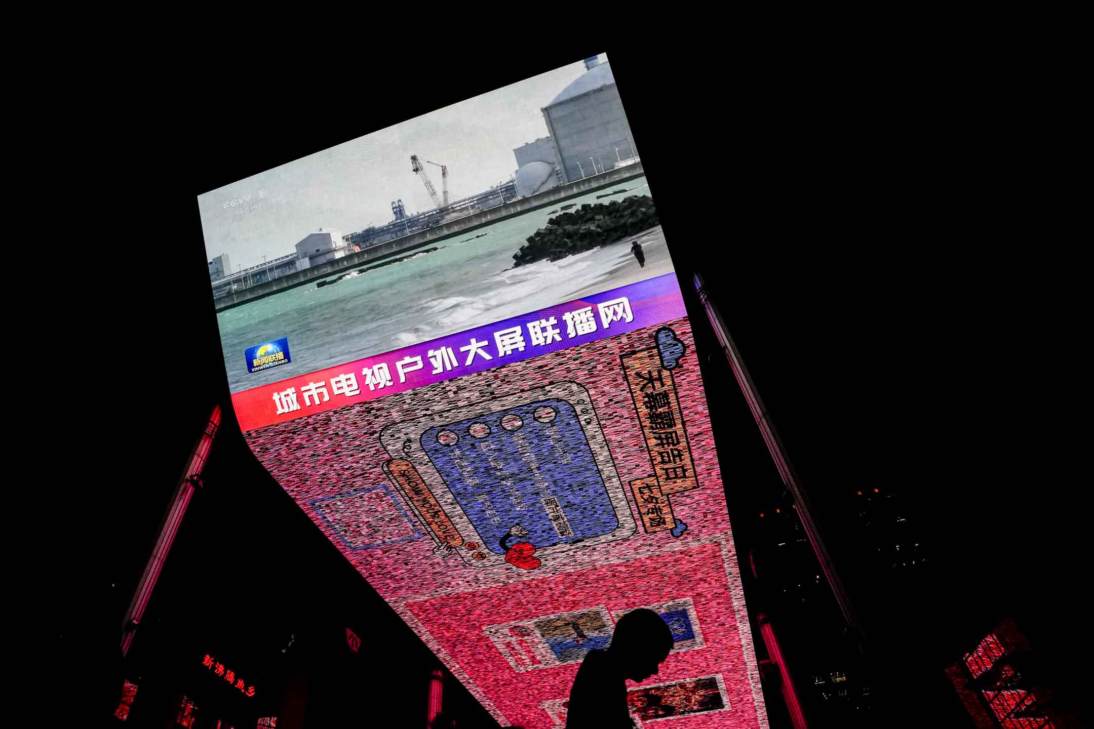 2023年8月24日,北京一名男子走过购物中心的大屏幕,中央电视台正在播放福岛第一核电站开始向太平洋释放第一批经过处理的放射性废水新闻。摄:Andy Wong/AP/达志影像